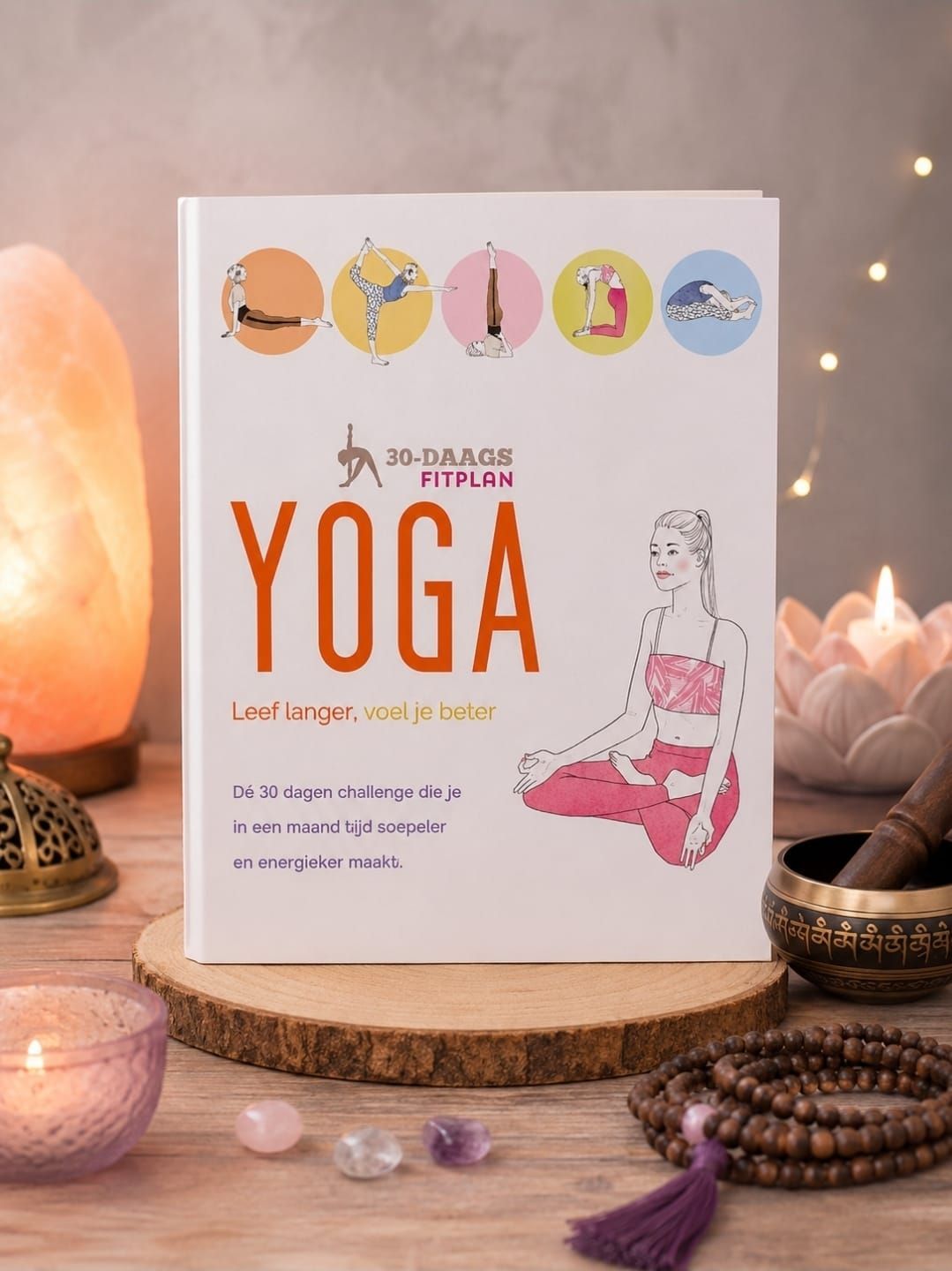 Een yogaboek met kleurrijke pictogrammen op een witte kaft, afgebeeld op een gezellig tafeltje met kaarsen en kralen.