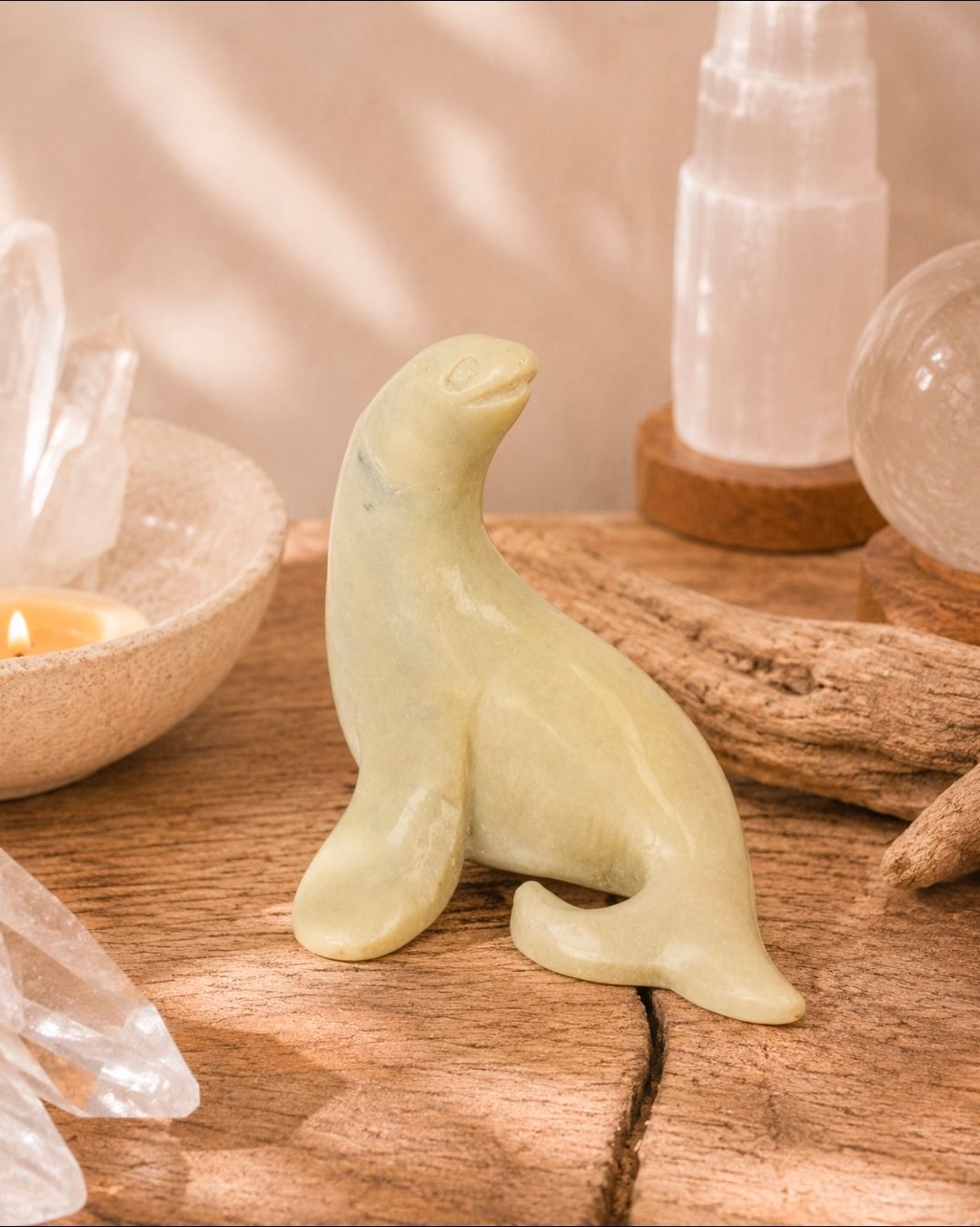 Klein, lichtgroen, gesneden zeehondbeeldje op een houten ondergrond naast kristallen en kaarsen.