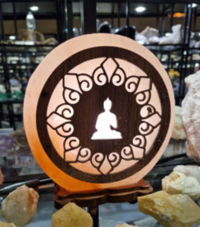 Een stralend Boeddha-silhouet in een ronde, uit hout gesneden lamp met warm oranje licht, tentoongesteld op een plank.