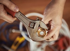 Hands using an adjustable wrench to tighten a brass fitting on a pipe