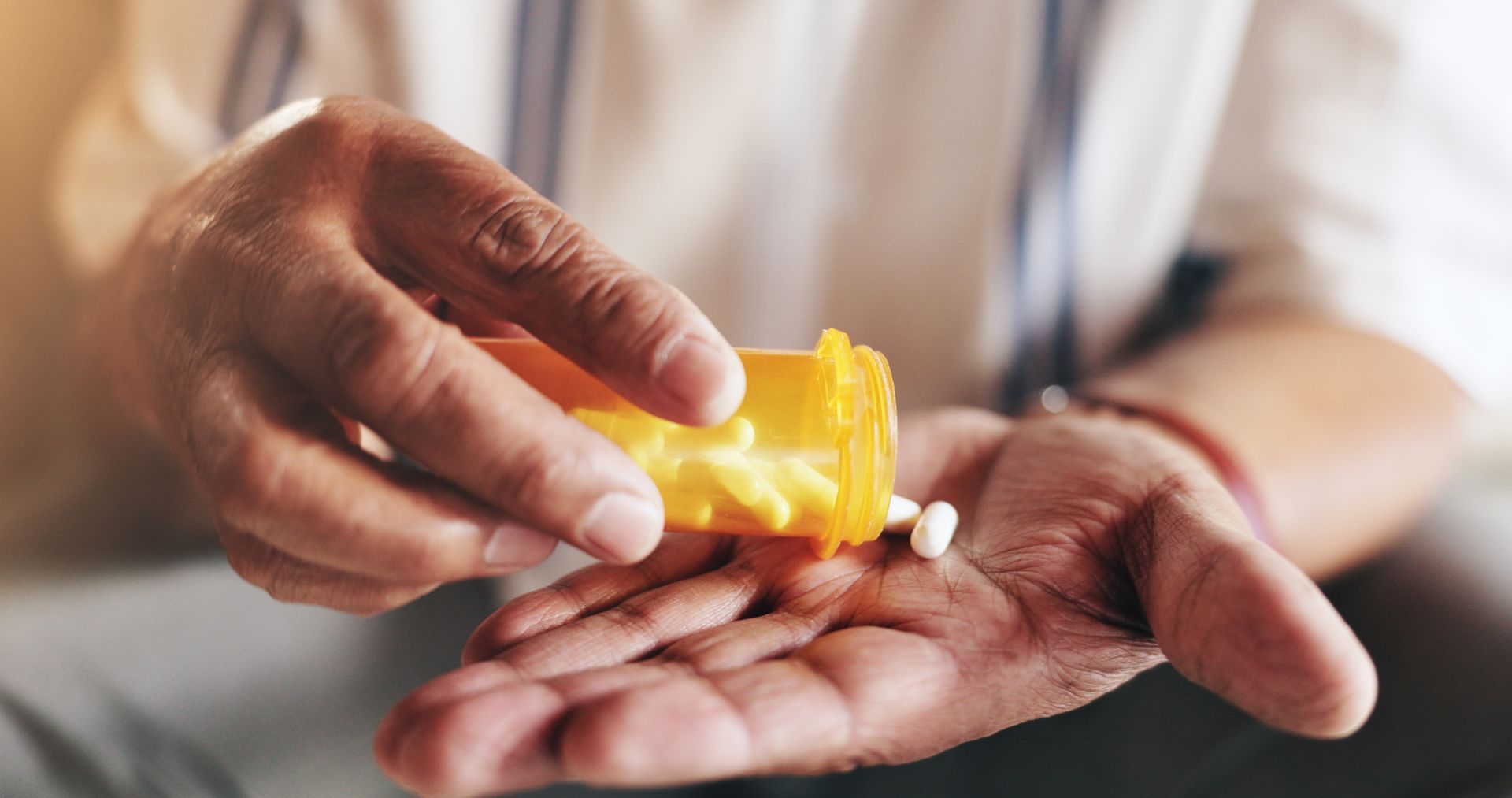 Person pouring pills from a yellow prescription bottle into their hand.