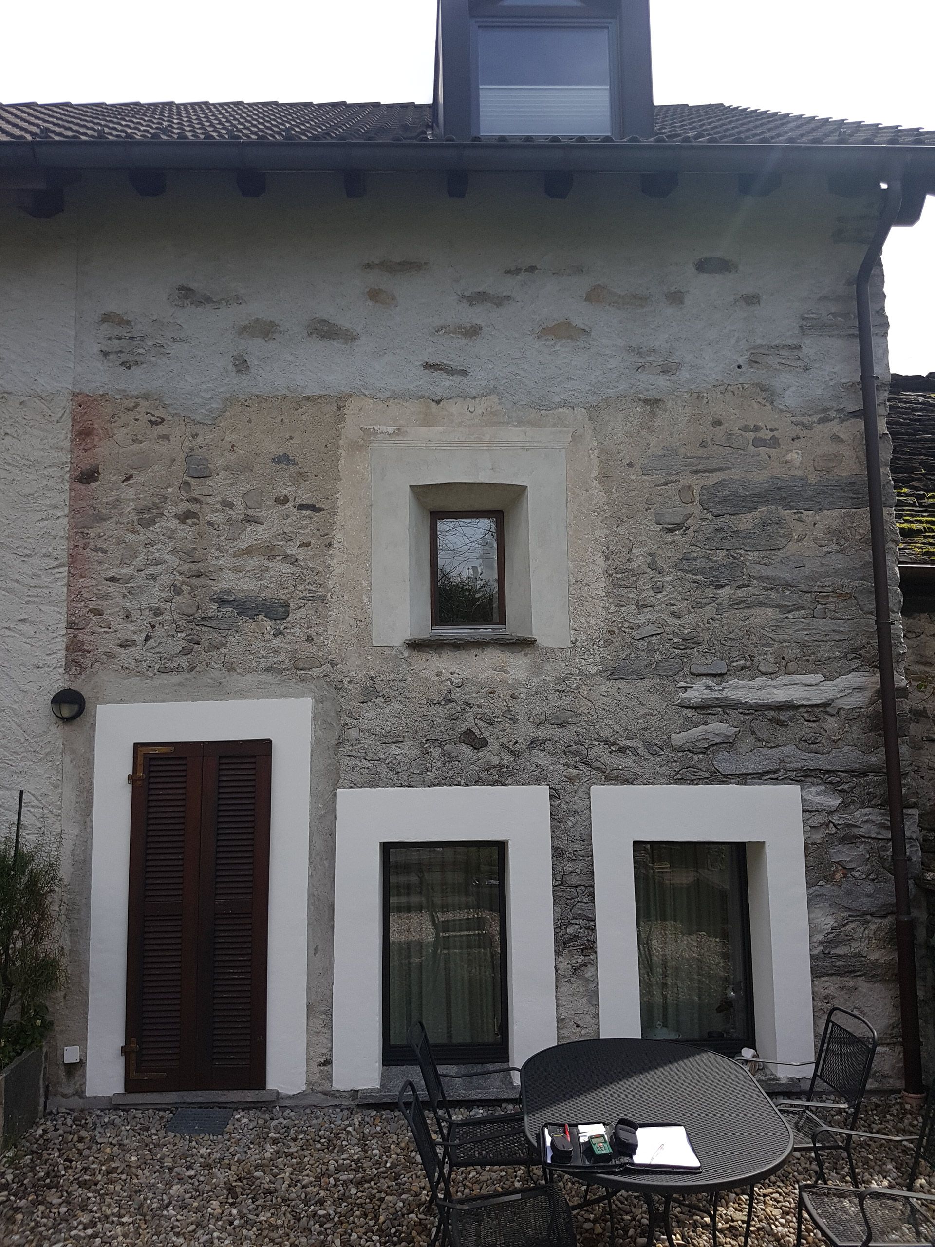 Un edificio in pietra con finestre con cornice bianca e davanti un tavolo e sedie