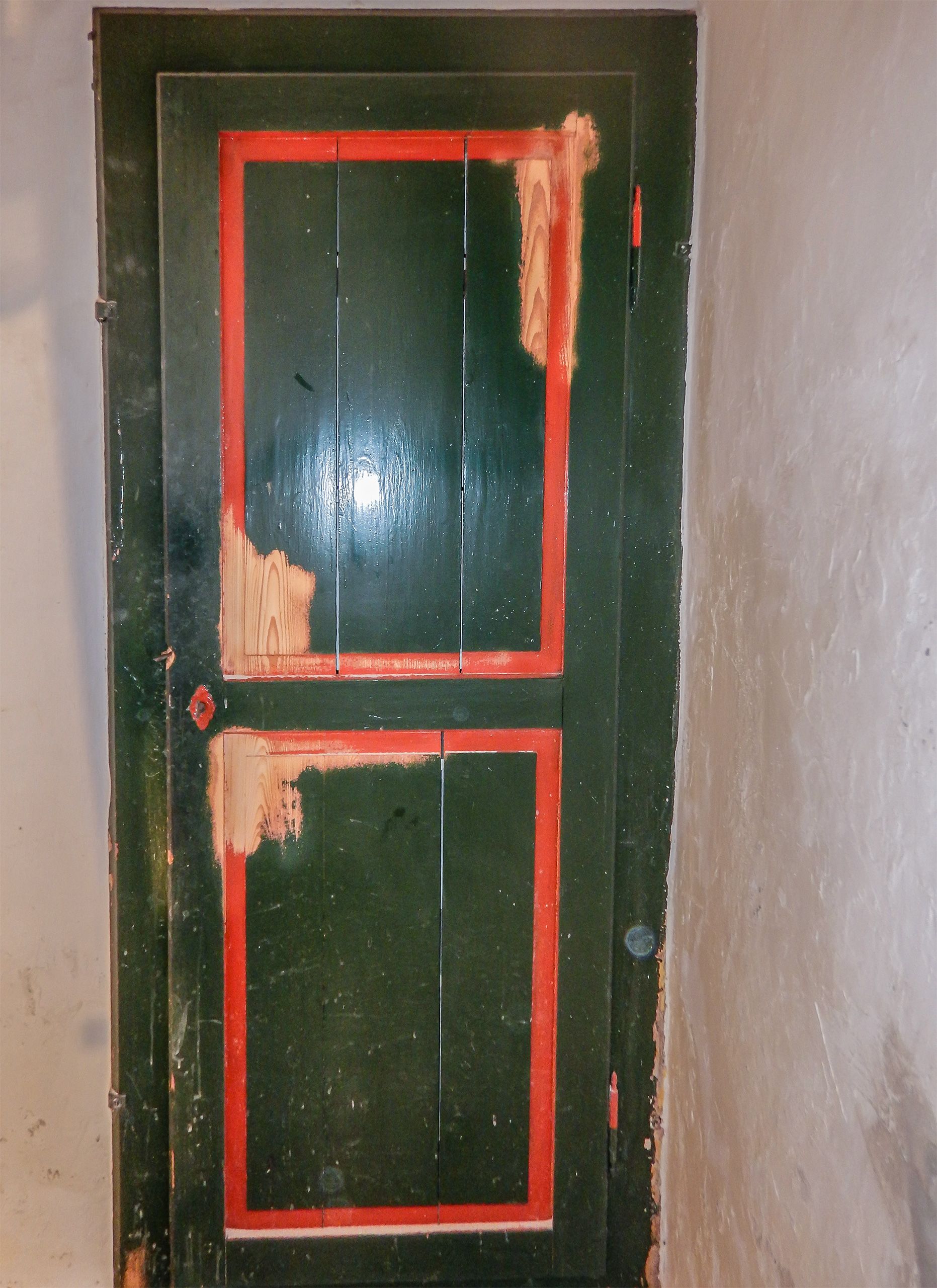 Una porta verde con un bordo rosso è contro un muro bianco