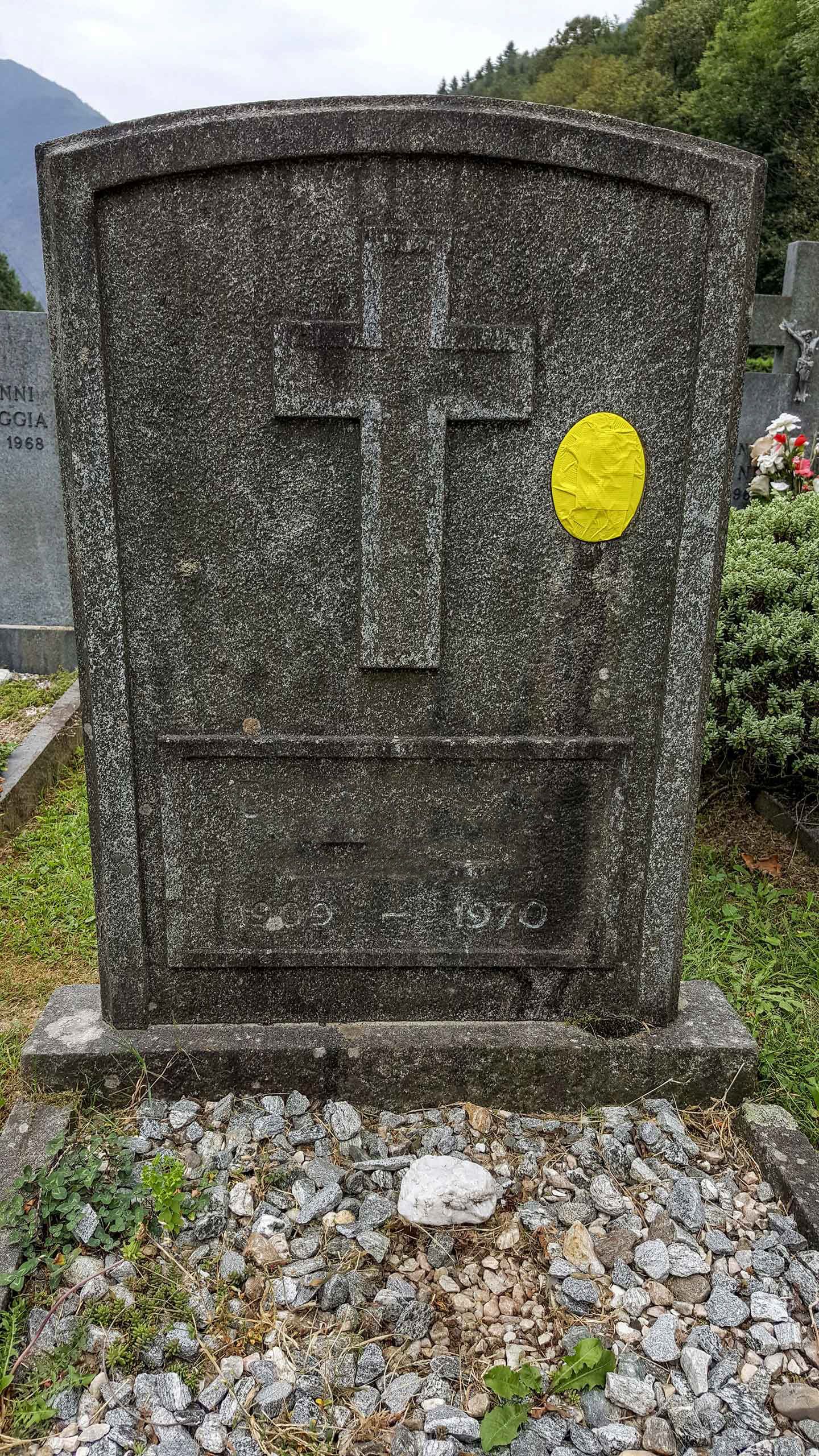 Una tomba con un fiore giallo sopra in un cimitero.