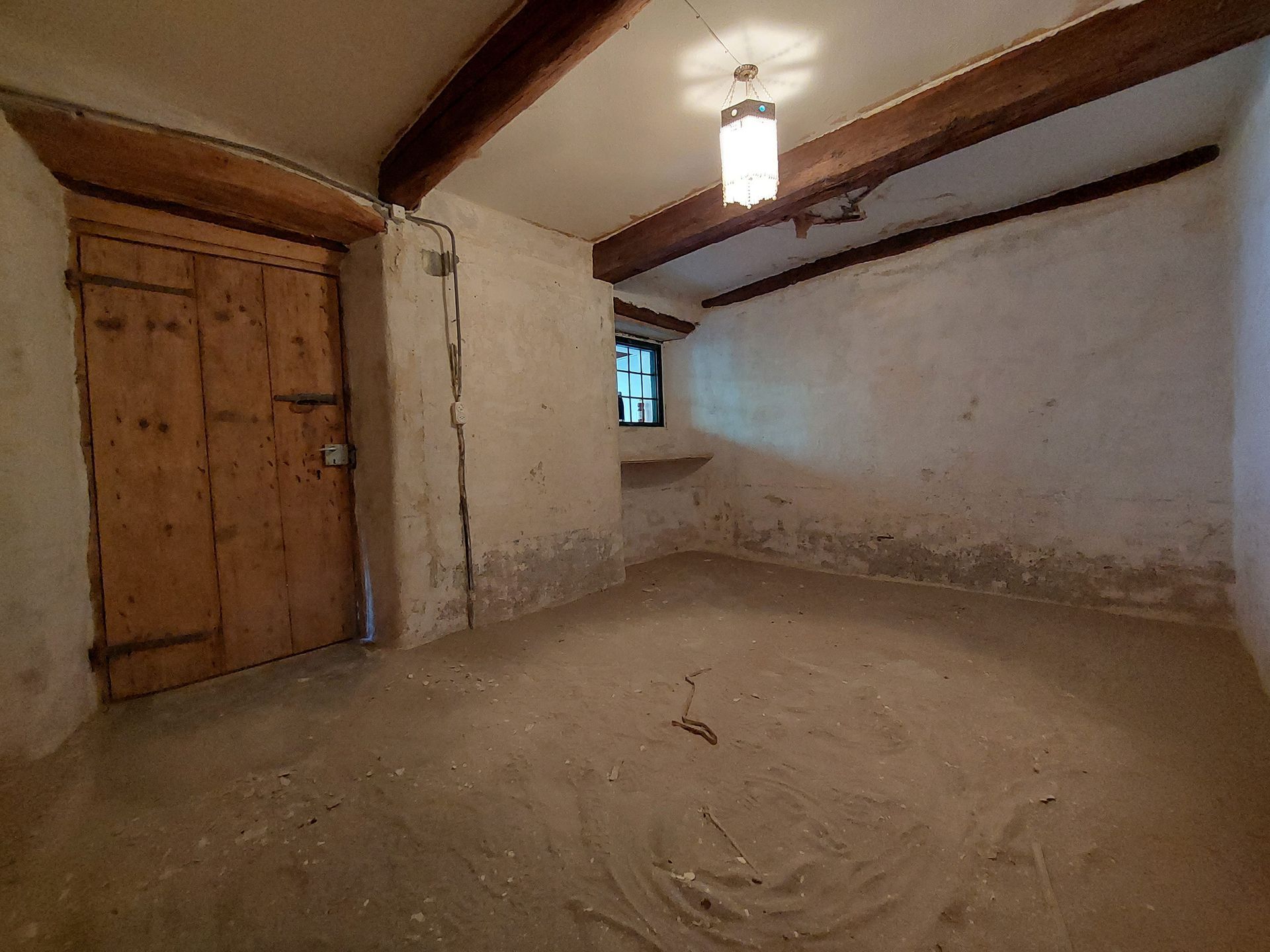 Una stanza vecchia vuota con una porta di legno e una lampada che pende dal soffitto