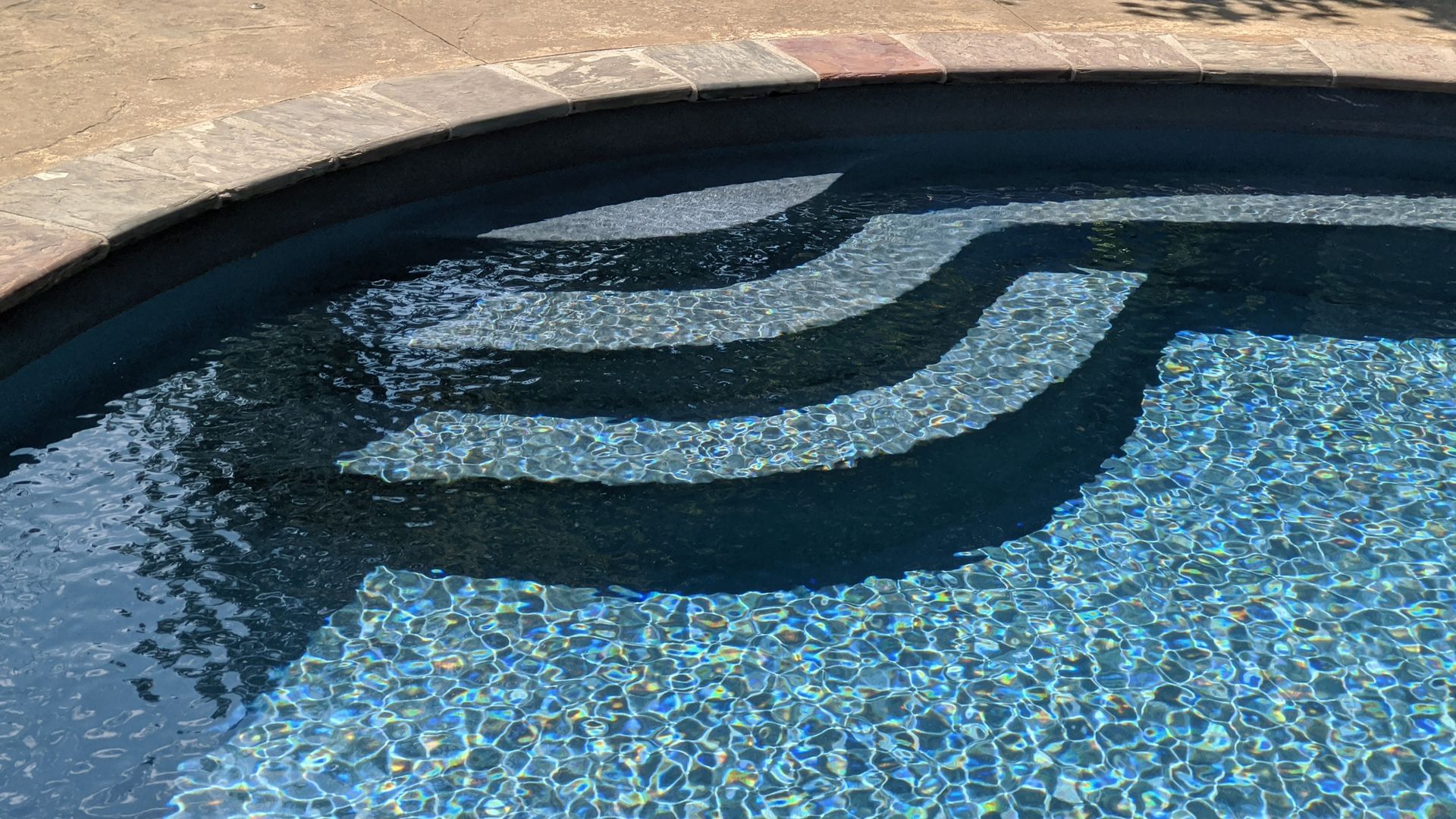 A swimmer in a blue pool swims toward the camera; water ripples around.