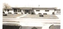 A single-story building with a flat roof, large windows, and a manicured lawn.
