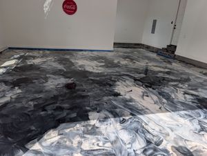 Partially coated room floor with dark epoxy swirls and a white wall in the background
