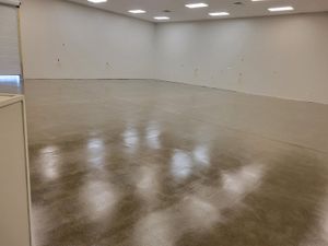 Empty beige room with glossy concrete floor and overhead lights reflecting off it