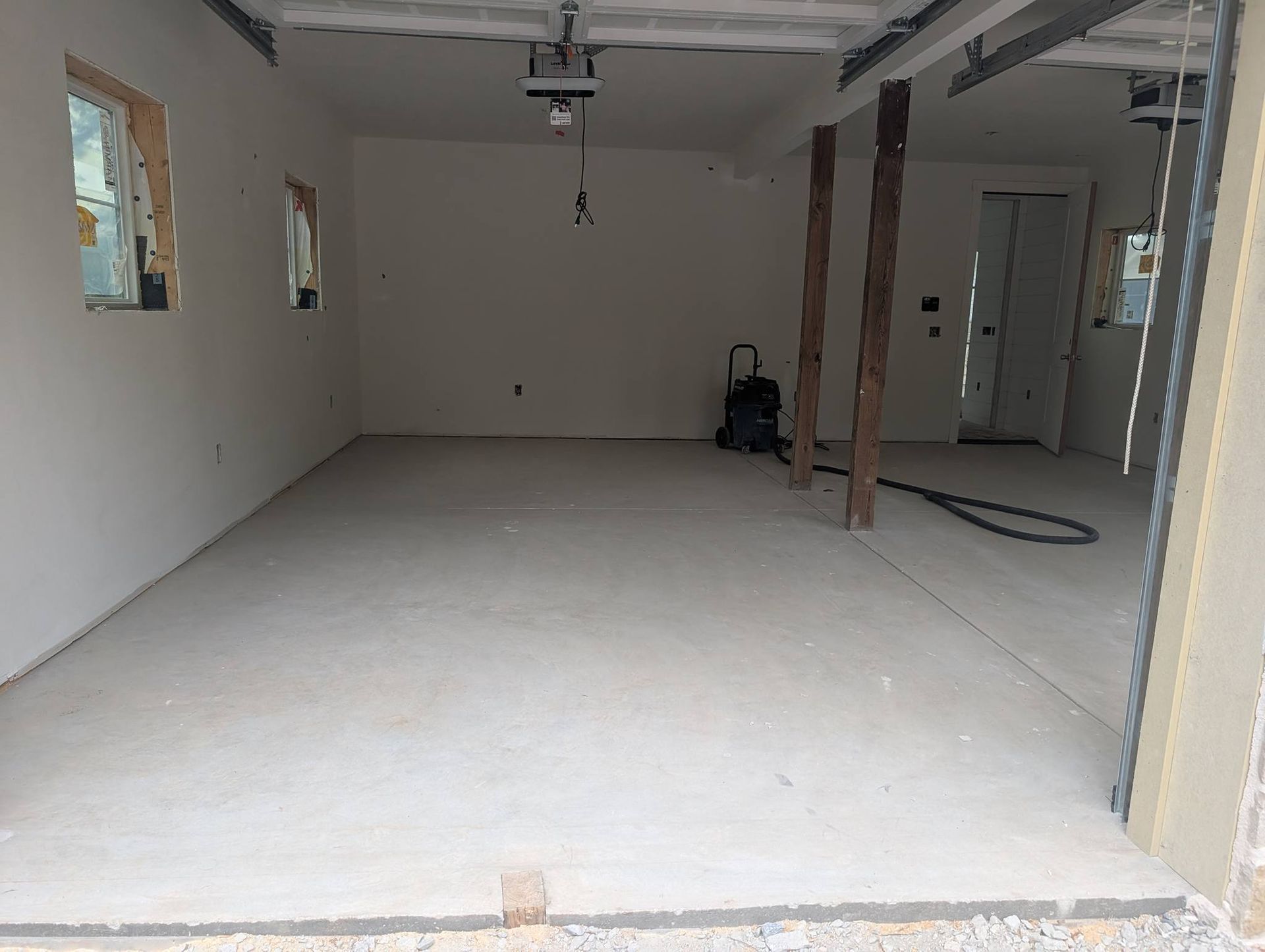 Empty unfinished garage interior with white walls, concrete floor, and exposed ceiling beams.