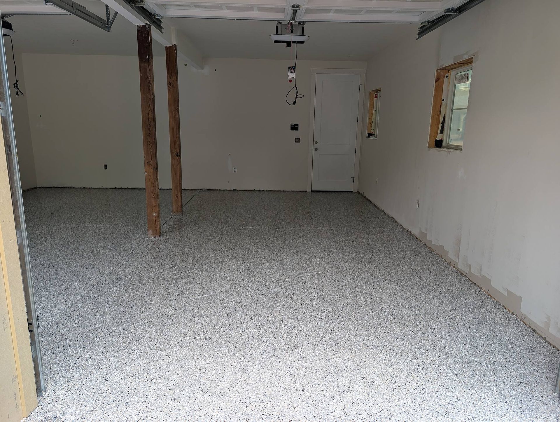 Empty unfinished basement with white walls, gray speckled floor, exposed posts, and a small window.