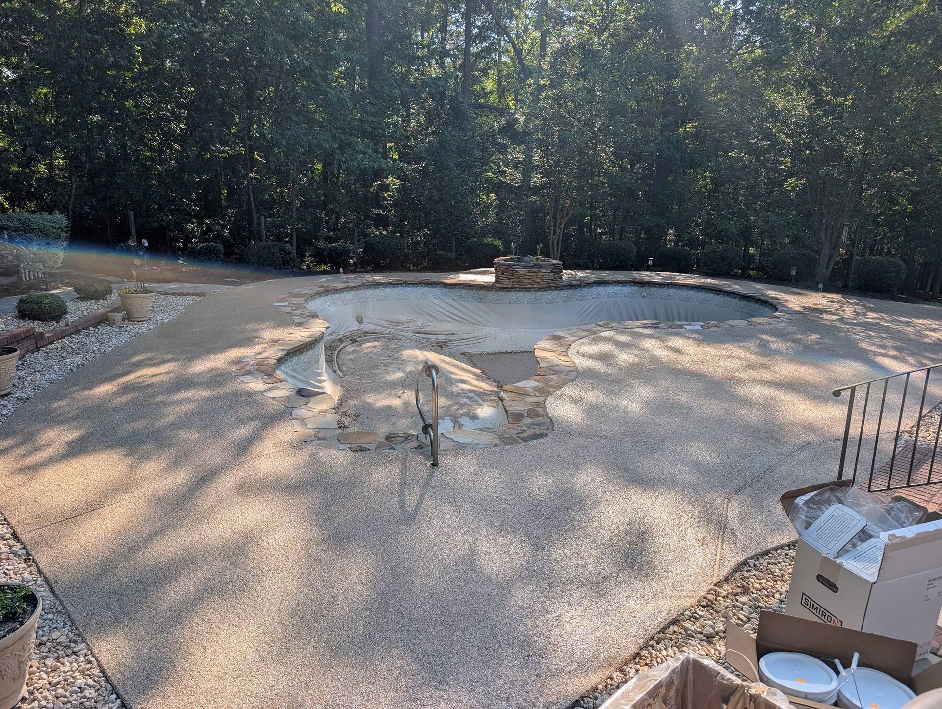 Outdoor patio under construction with gravel ground, curved stone edging, and trees in the background