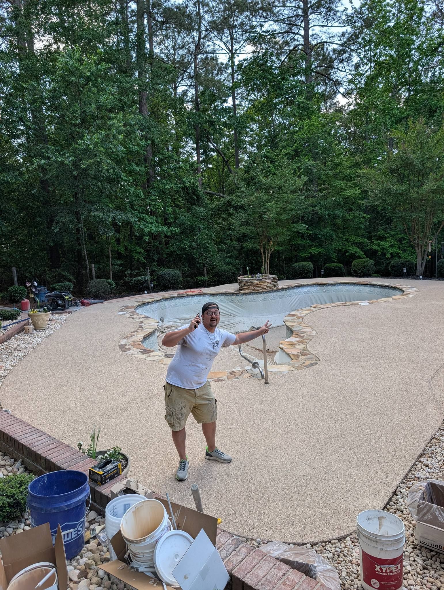 Person standing in a gravel-filled backyard beside a shallow pond, holding a small dog on a leash