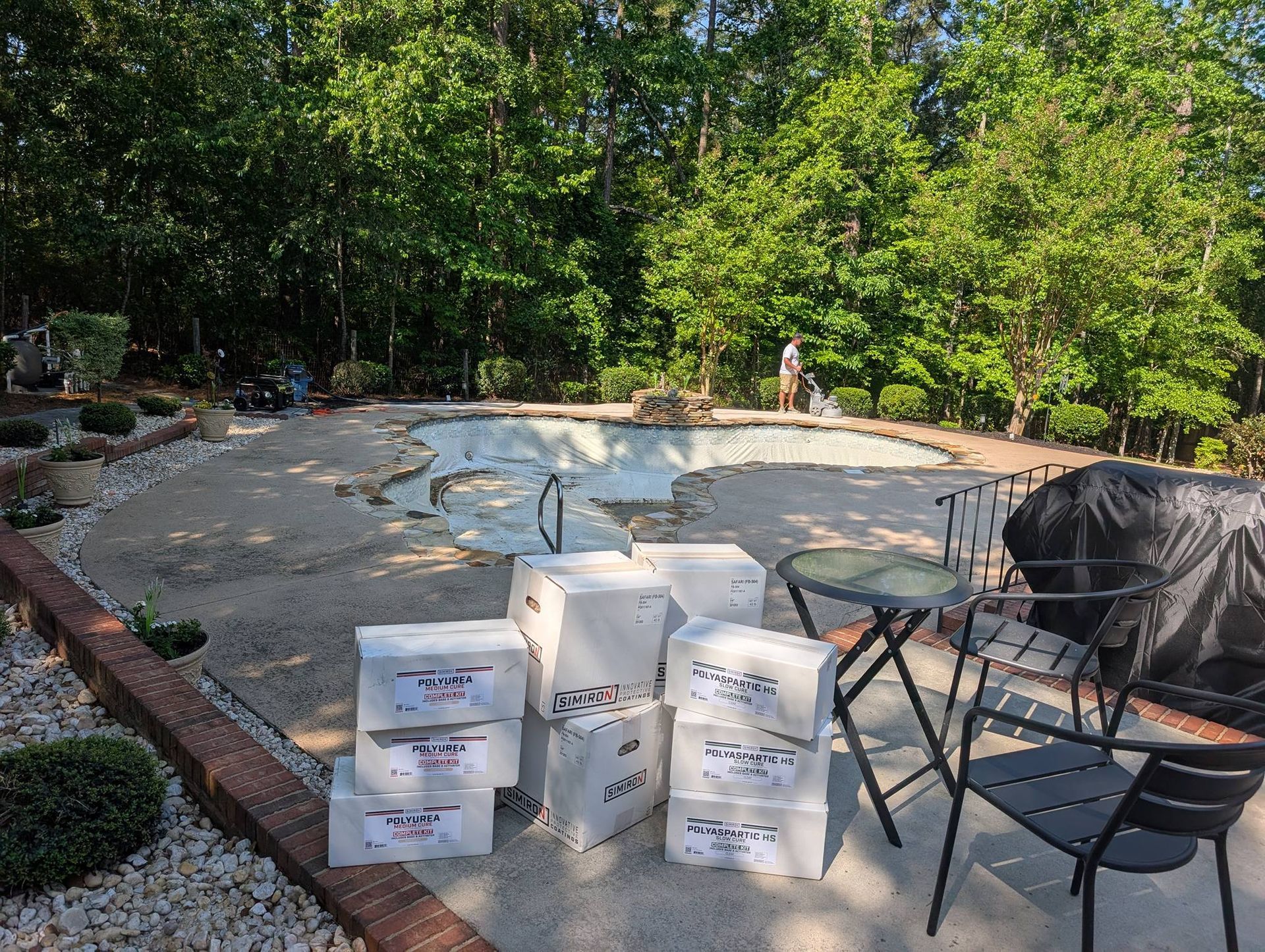 Backyard pool under renovation with stacked white bags and covered patio chairs beside it