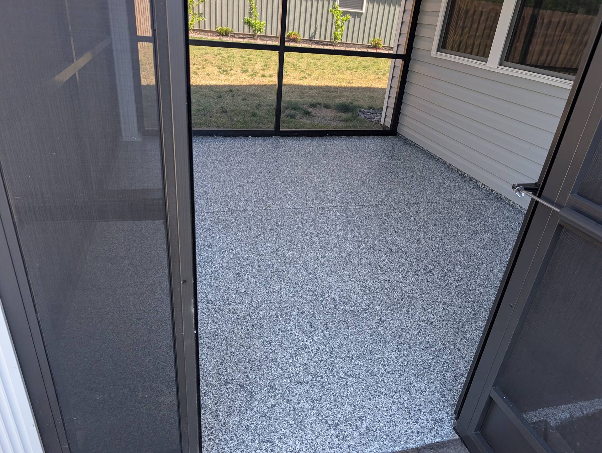 Screened patio with gray speckled floor, black mesh doors, and a view of the yard outside