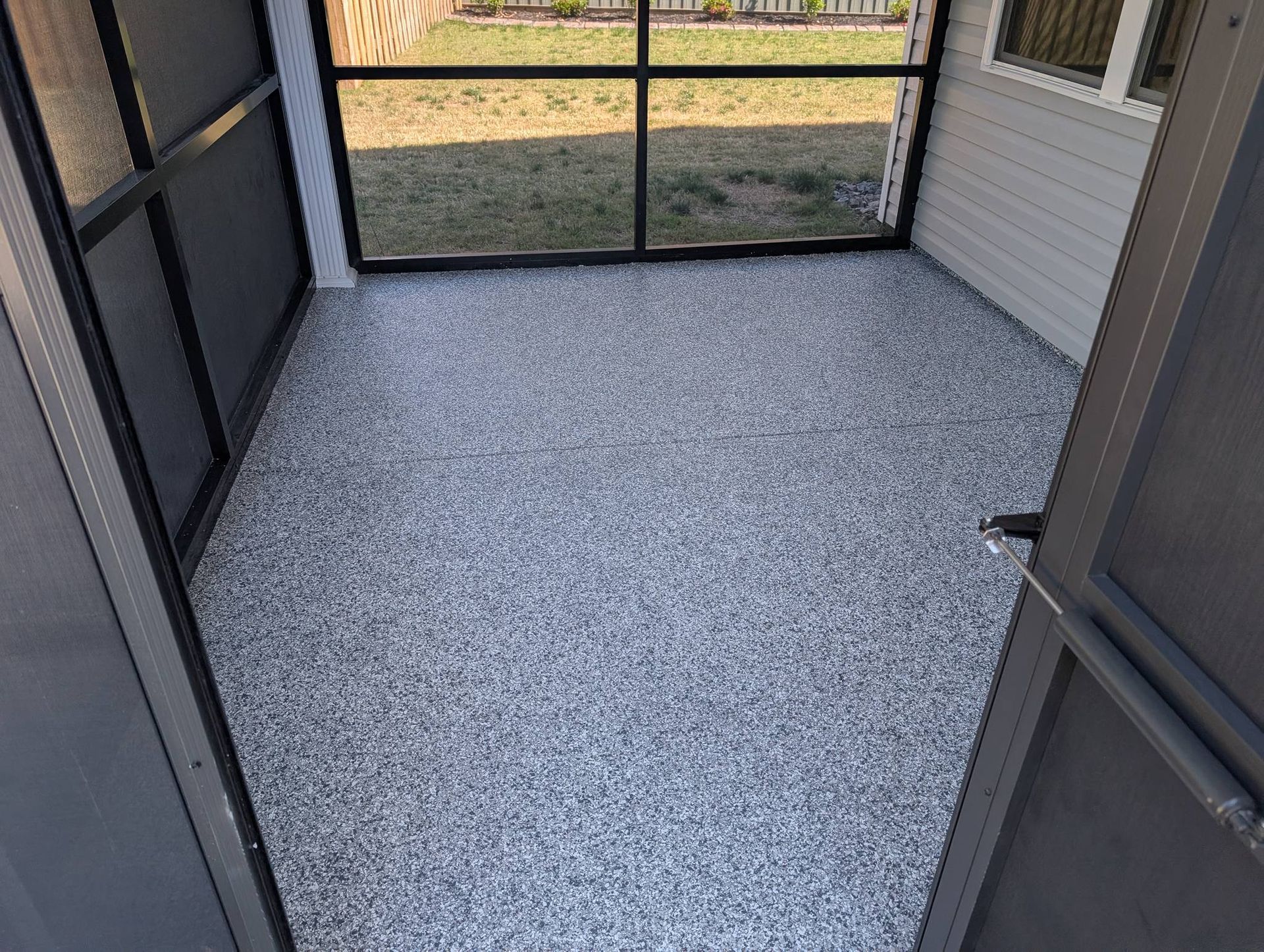 Enclosed screened patio with gray speckled floor and black mesh walls, opening to a yard.