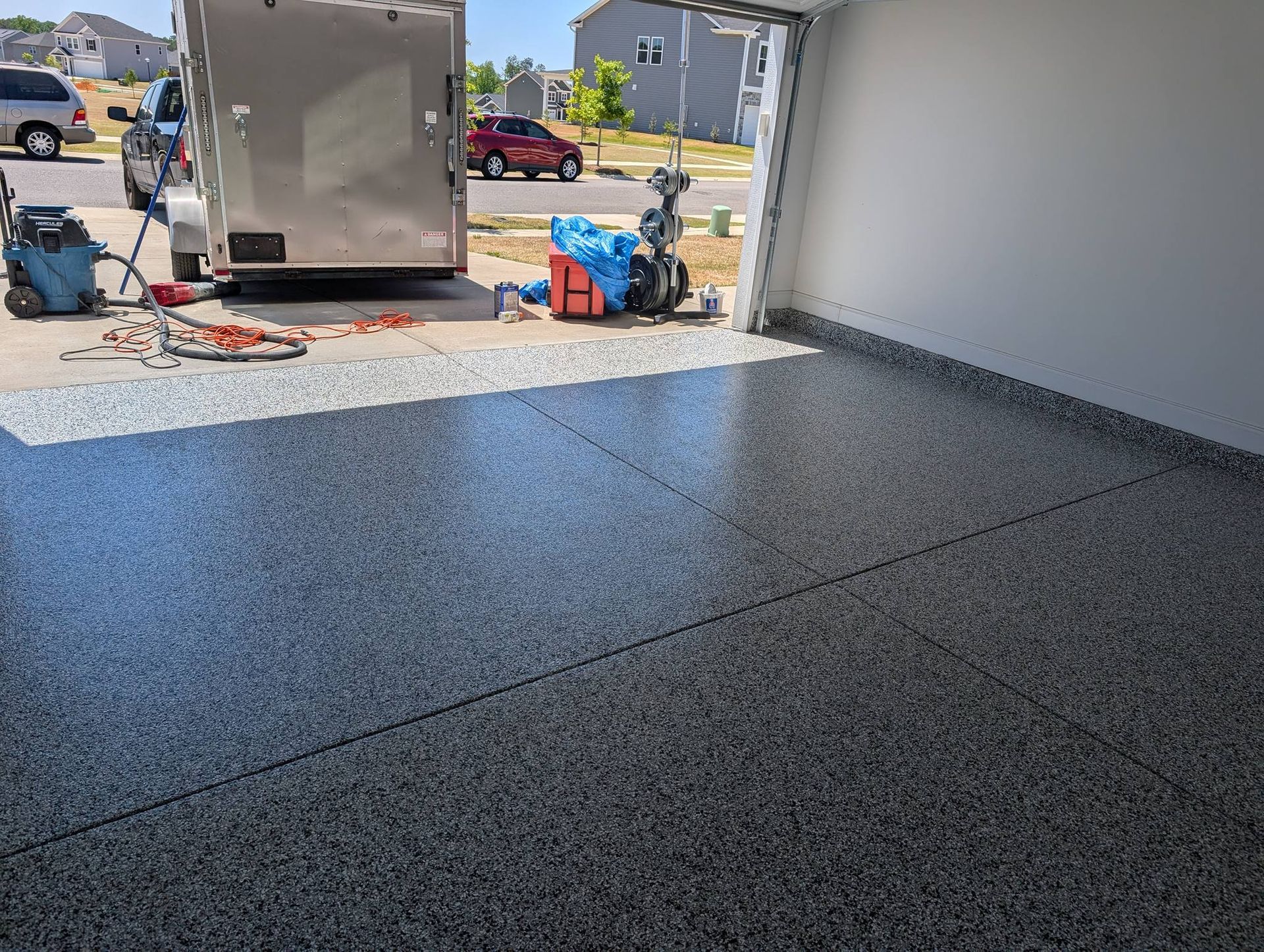 Freshly coated black epoxy garage floor with a trailer, tools, and a suburban driveway outside