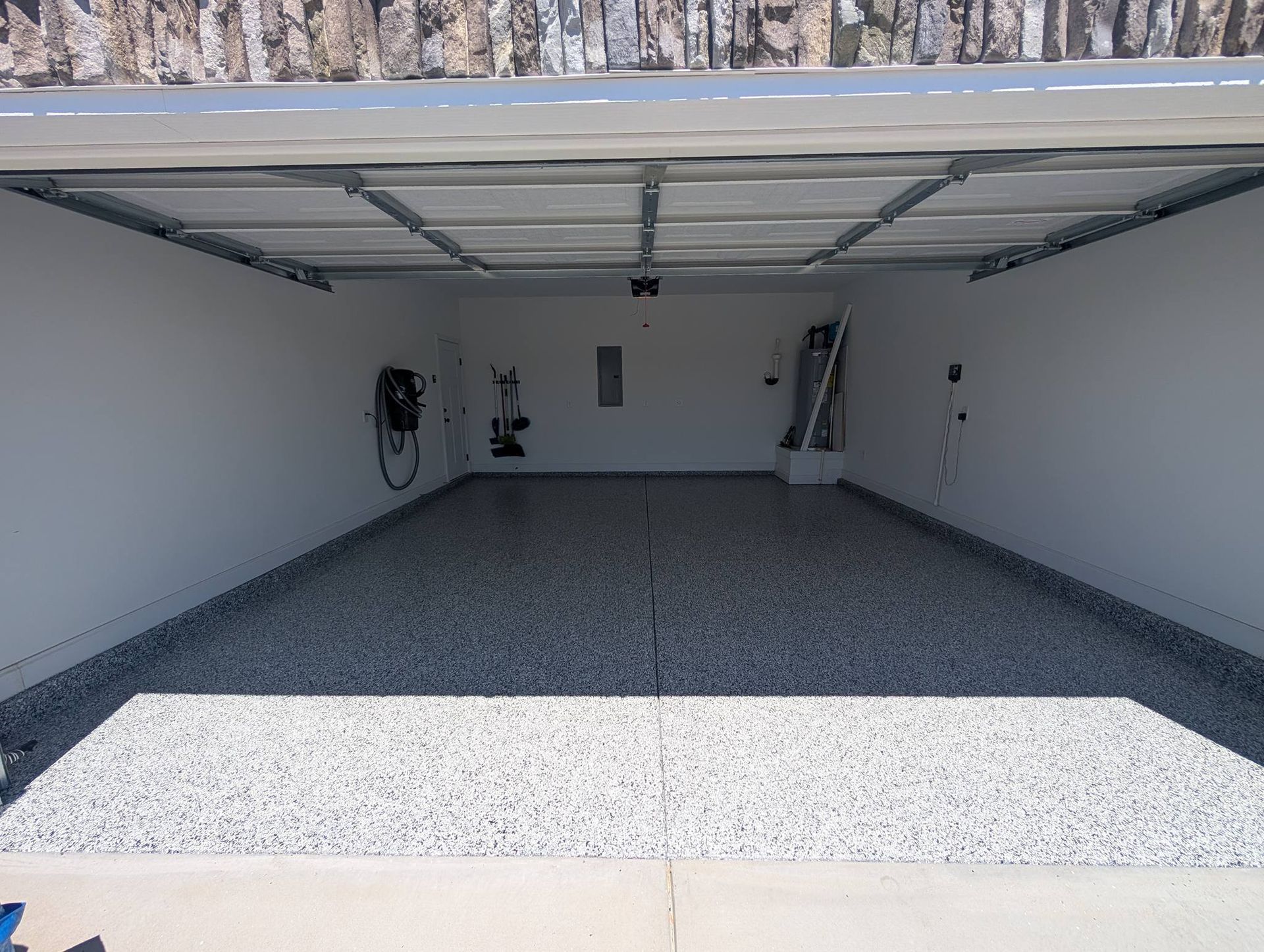 Open two-car garage with white walls, speckled floor, and raised overhead door.