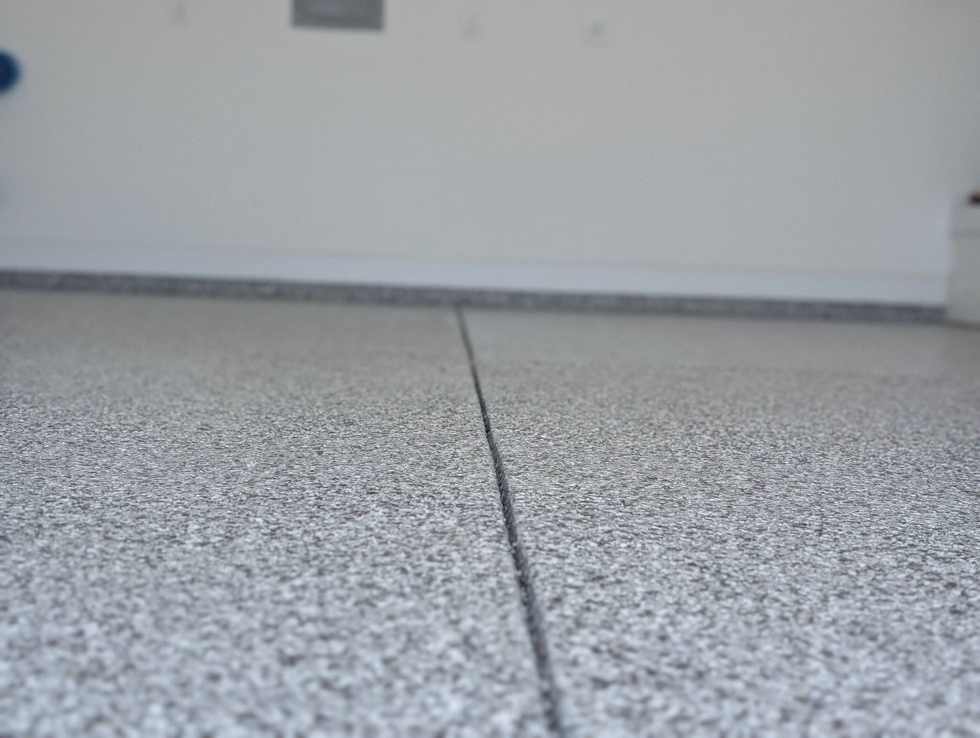 Close-up of a speckled gray floor with a dark seam leading toward a white wall