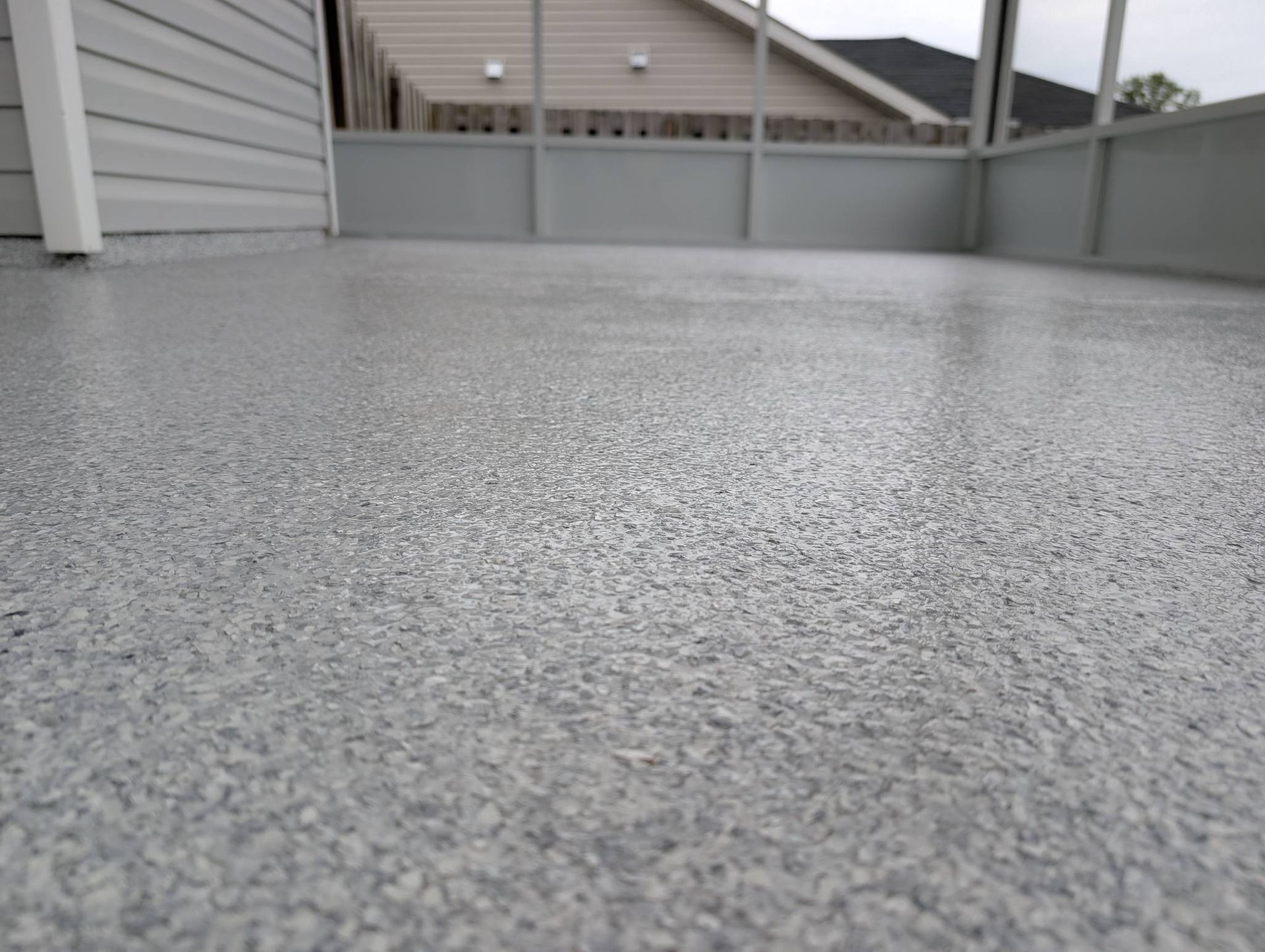 Wet gray concrete patio beside a fence and house siding under an overcast sky