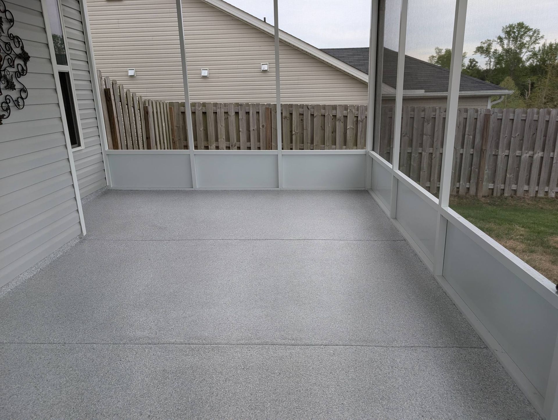 Covered concrete patio with gray half-walls and a wooden fence in a backyard.
