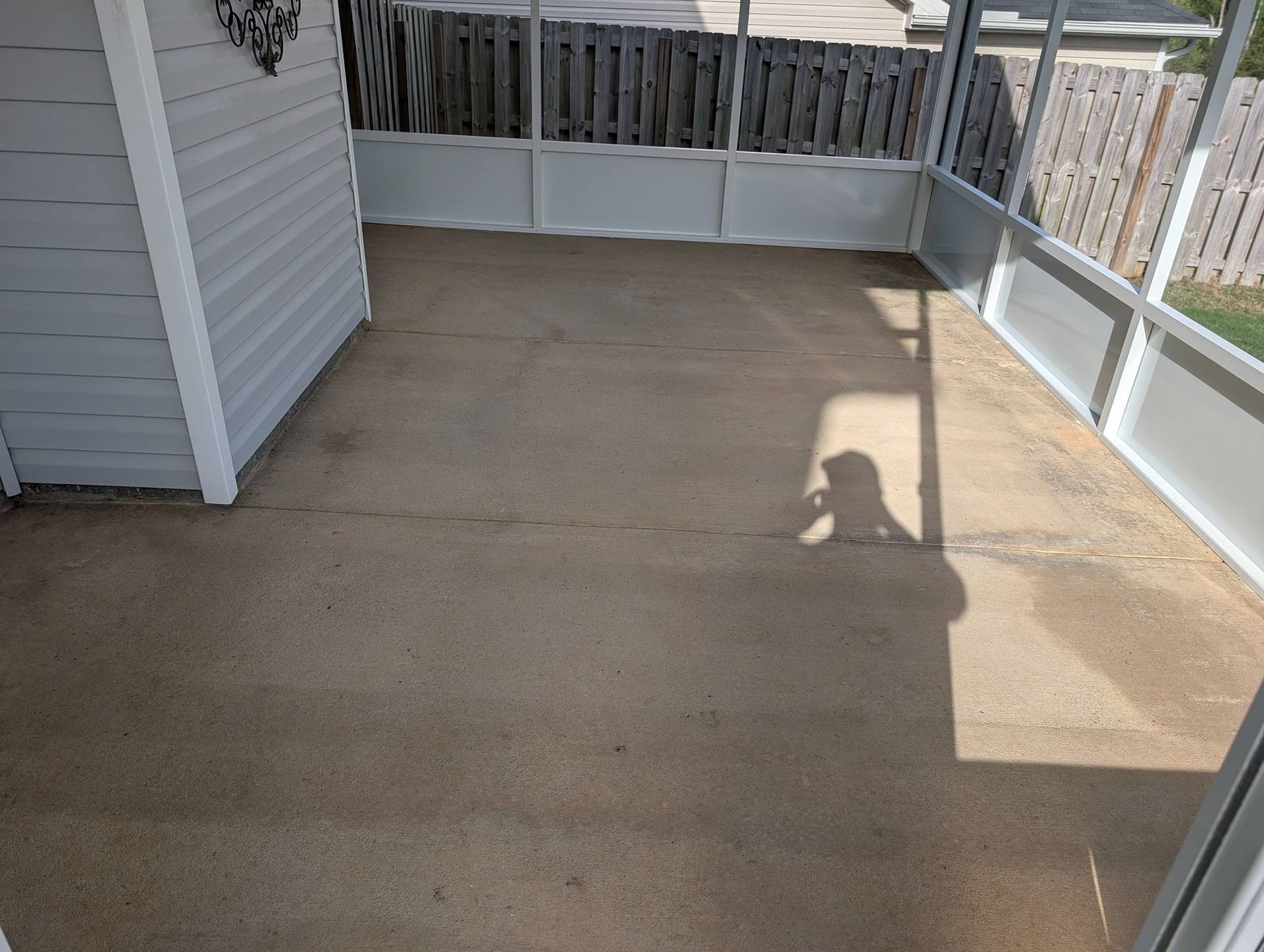 Sunlit concrete patio or balcony with white railing and a person’s shadow on the ground