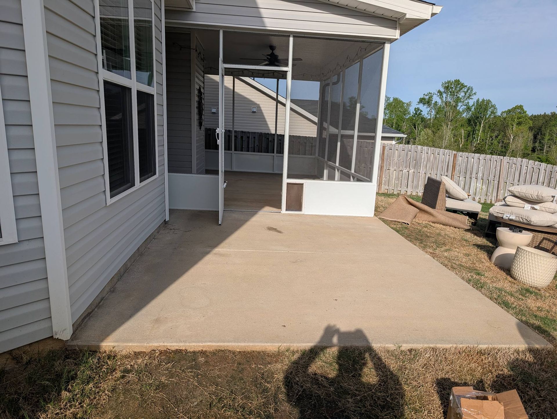Concrete patio beside gray house with screened porch and fenced yard