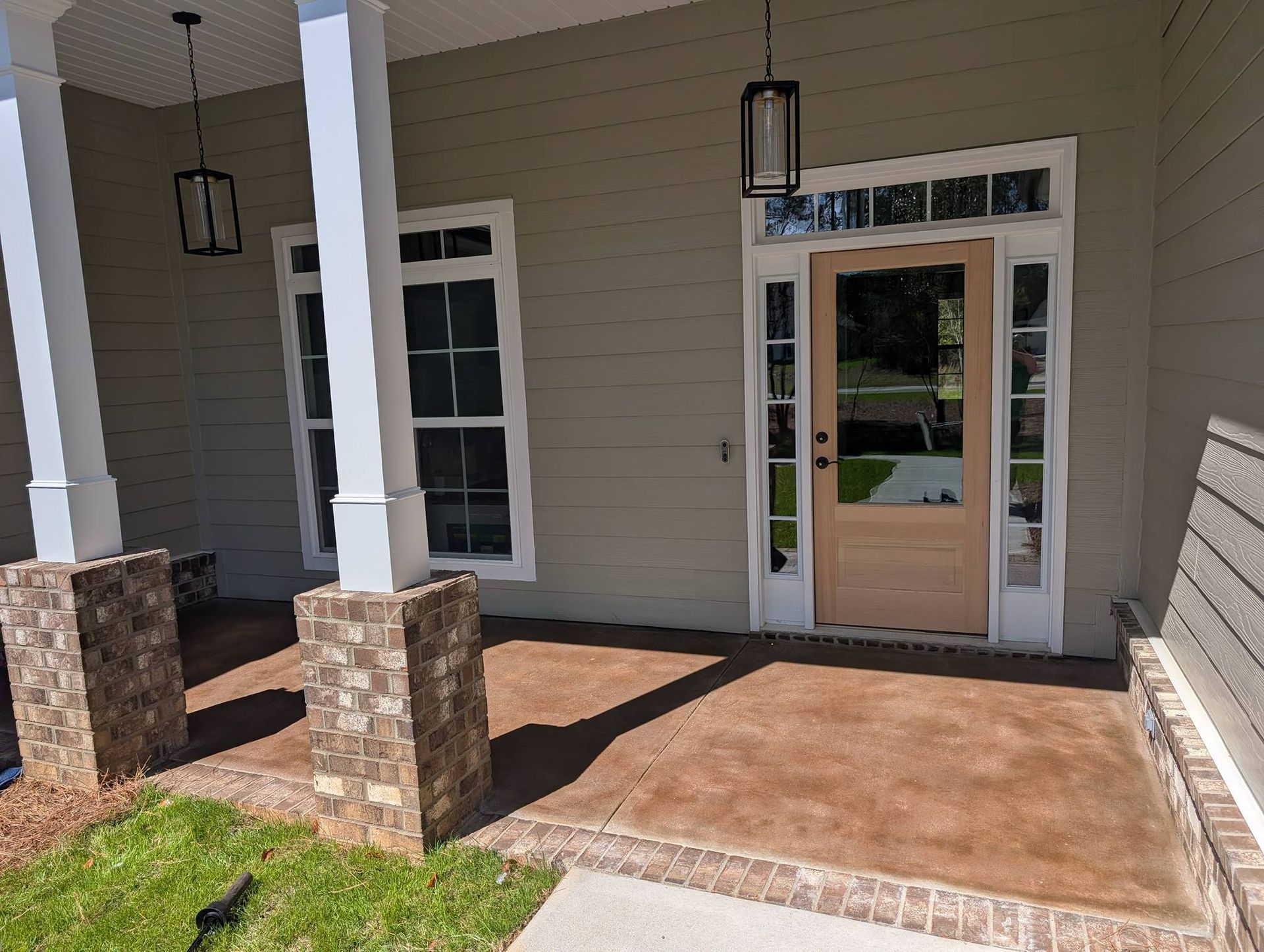 Covered building entrance with brick columns, tan siding, and double glass doors under a porch.