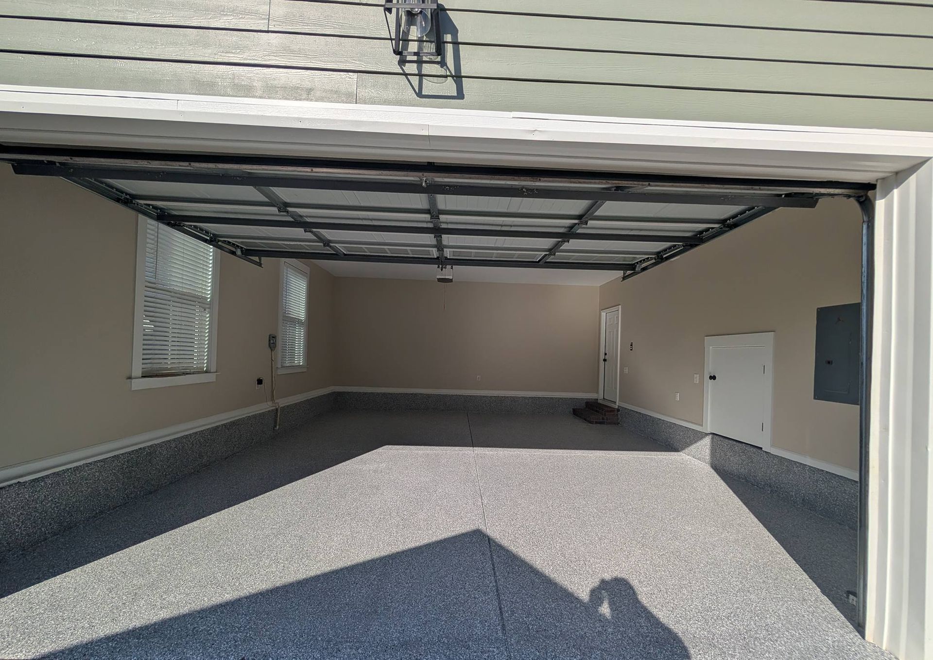Open garage with speckled floor, beige siding, and overhead door tracks visible.