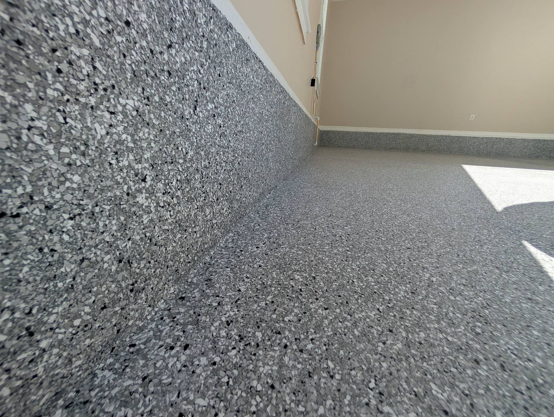 Speckled gray terrazzo floor beside a beige wall and bright sunlit opening