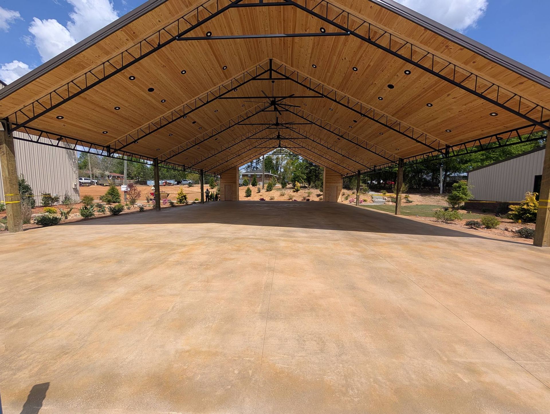 Large open-air pavilion with a wooden peaked roof over a concrete floor in an outdoor setting