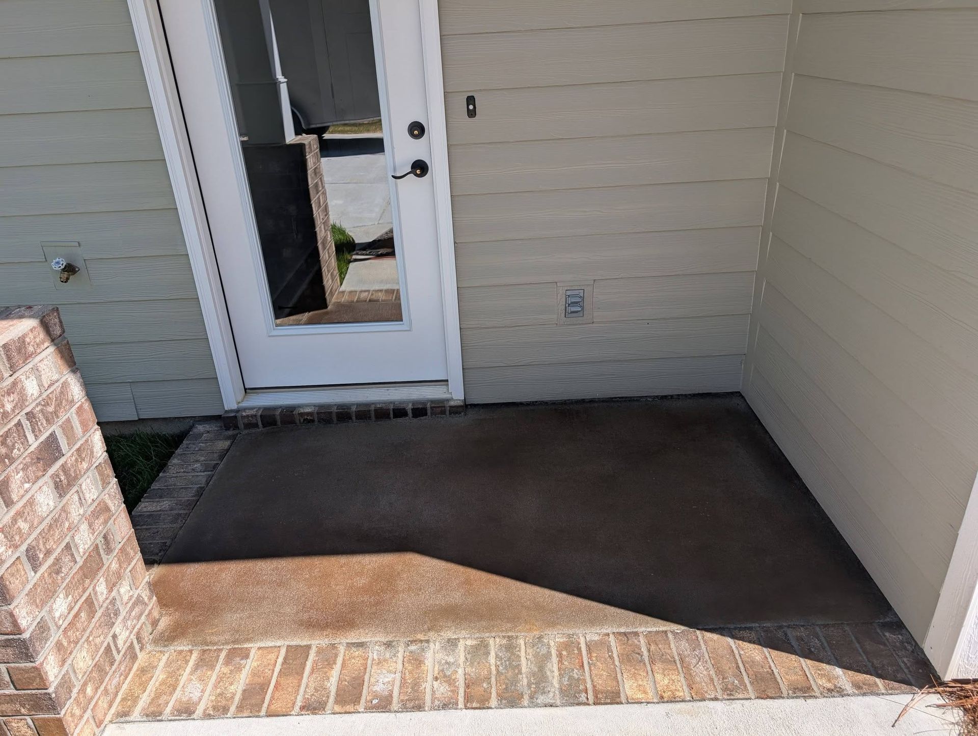 Small covered front porch with brick step and white door, showing a dark concrete floor.
