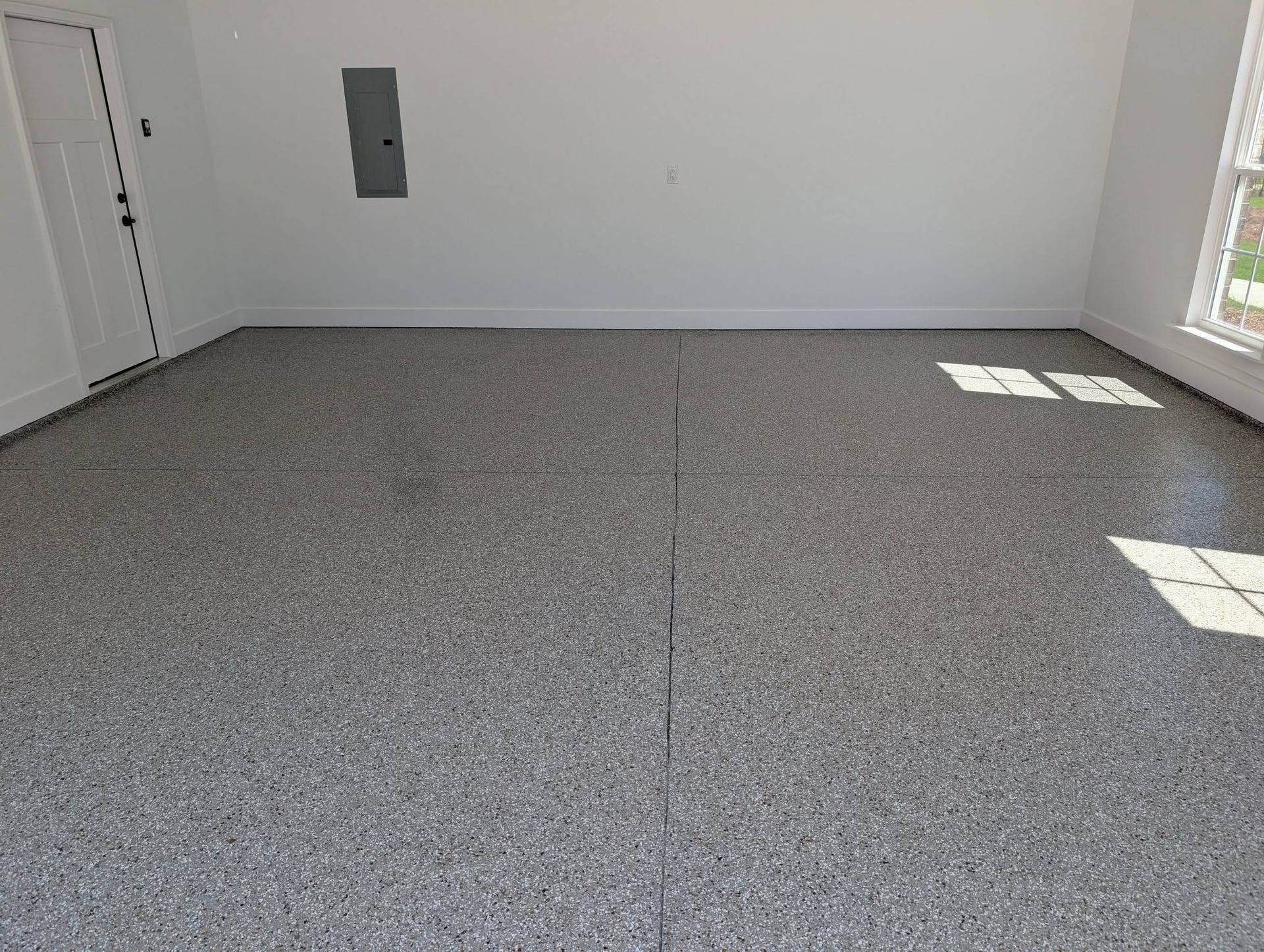 Empty gray-carpeted room with white walls and sunlight from a window on the right