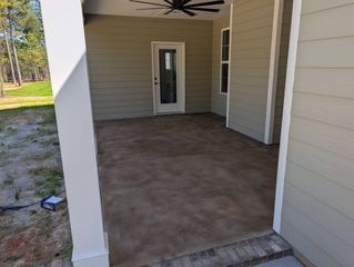Covered front porch with concrete floor and white siding, viewed toward a glass door.