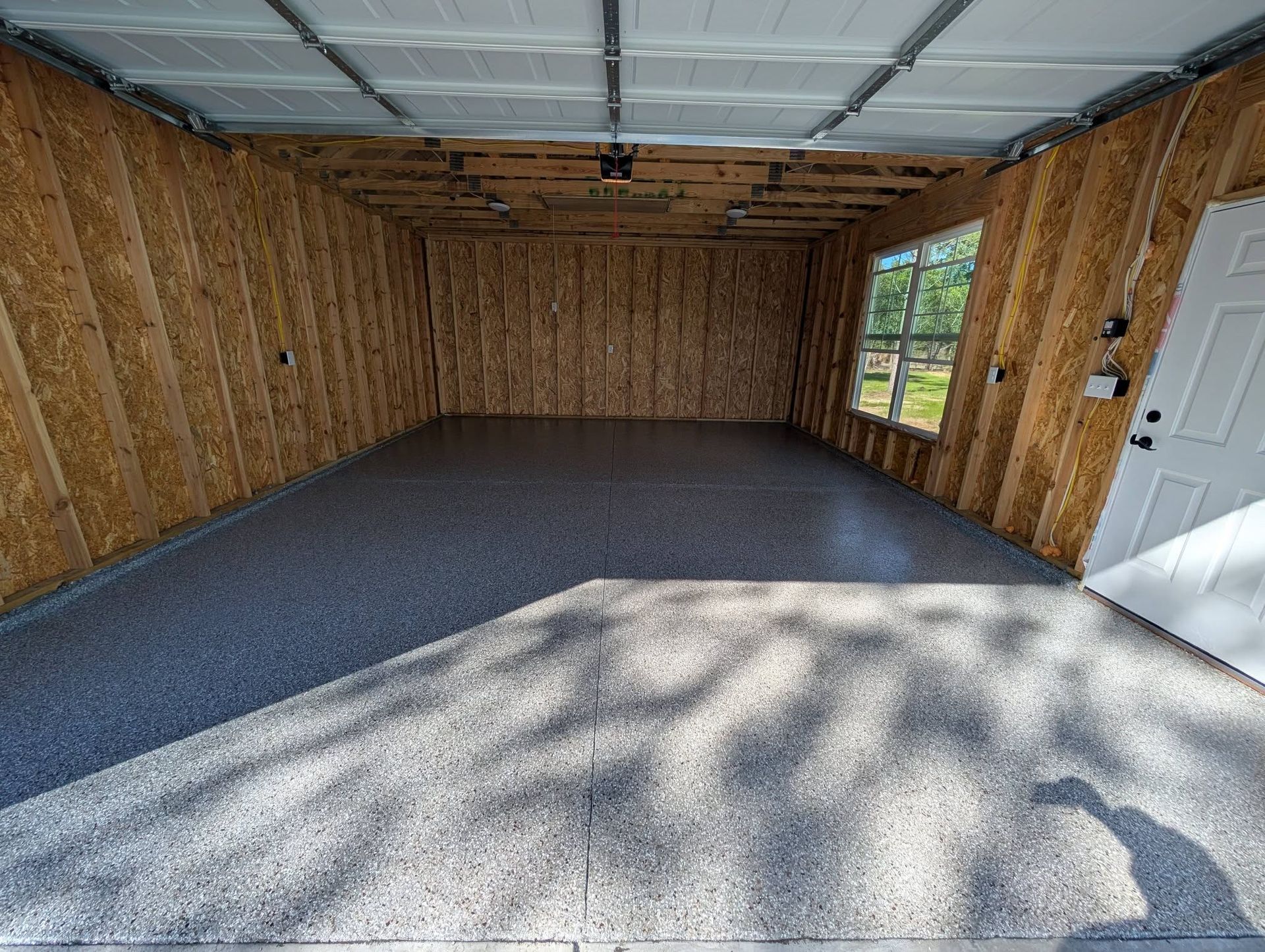 Empty unfinished garage interior with exposed wooden walls, concrete floor, and a white side door.