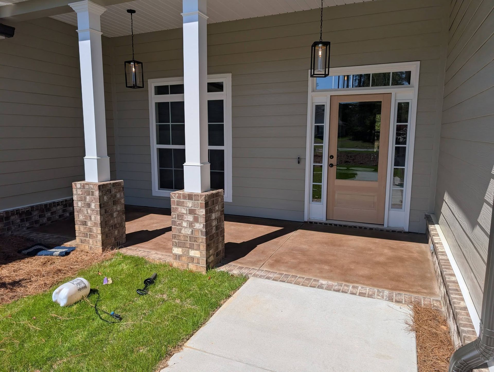 Front porch with white columns, stone bases, hanging lights, glass door, and a small grassy yard.