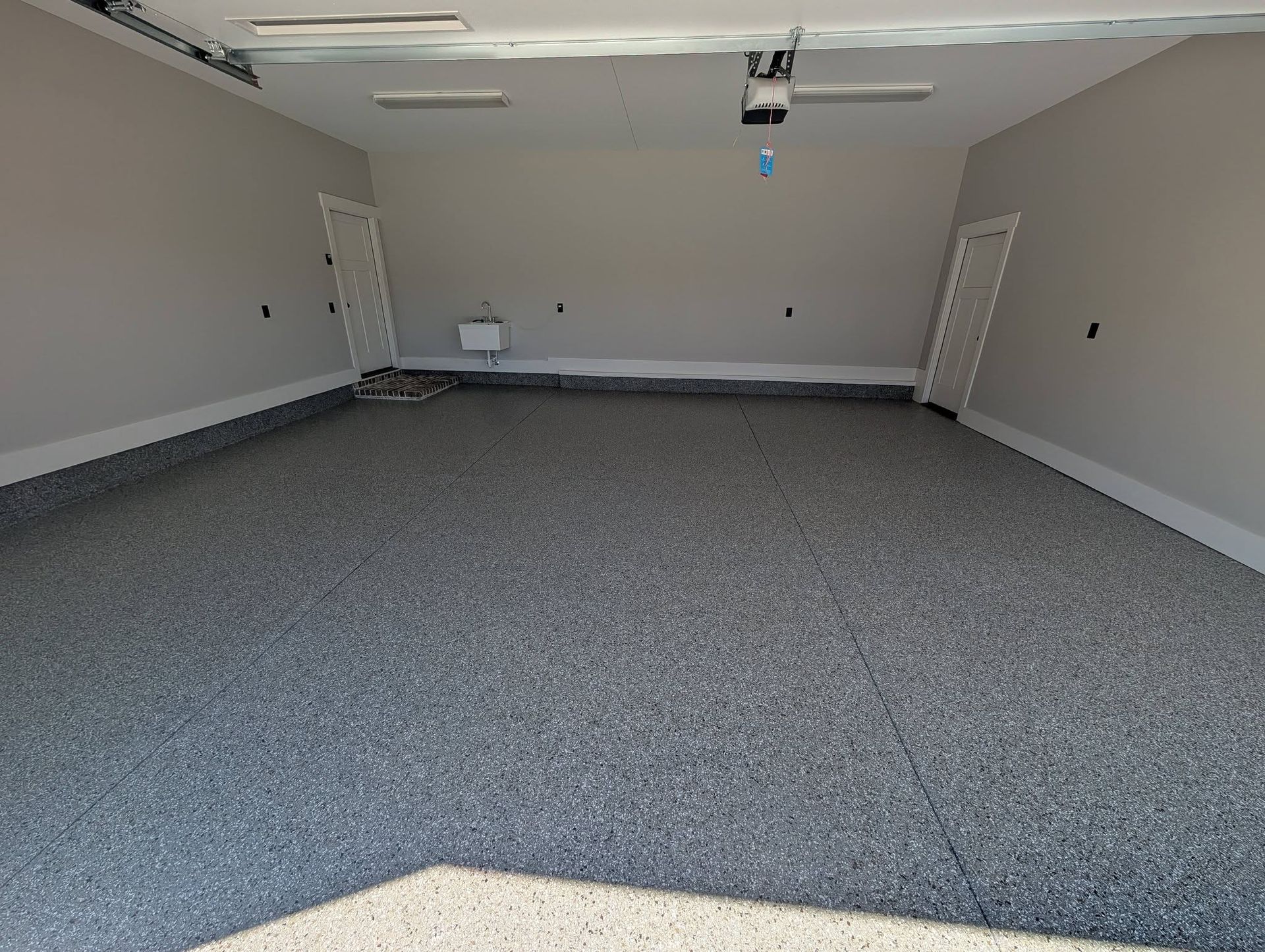 Empty gray-carpeted garage with white walls, ceiling lights, and a garage door opener.