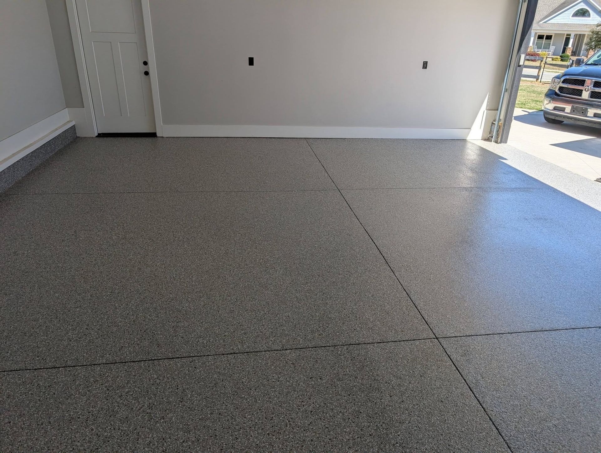 Empty garage with freshly painted speckled concrete floor and open doorway to the driveway