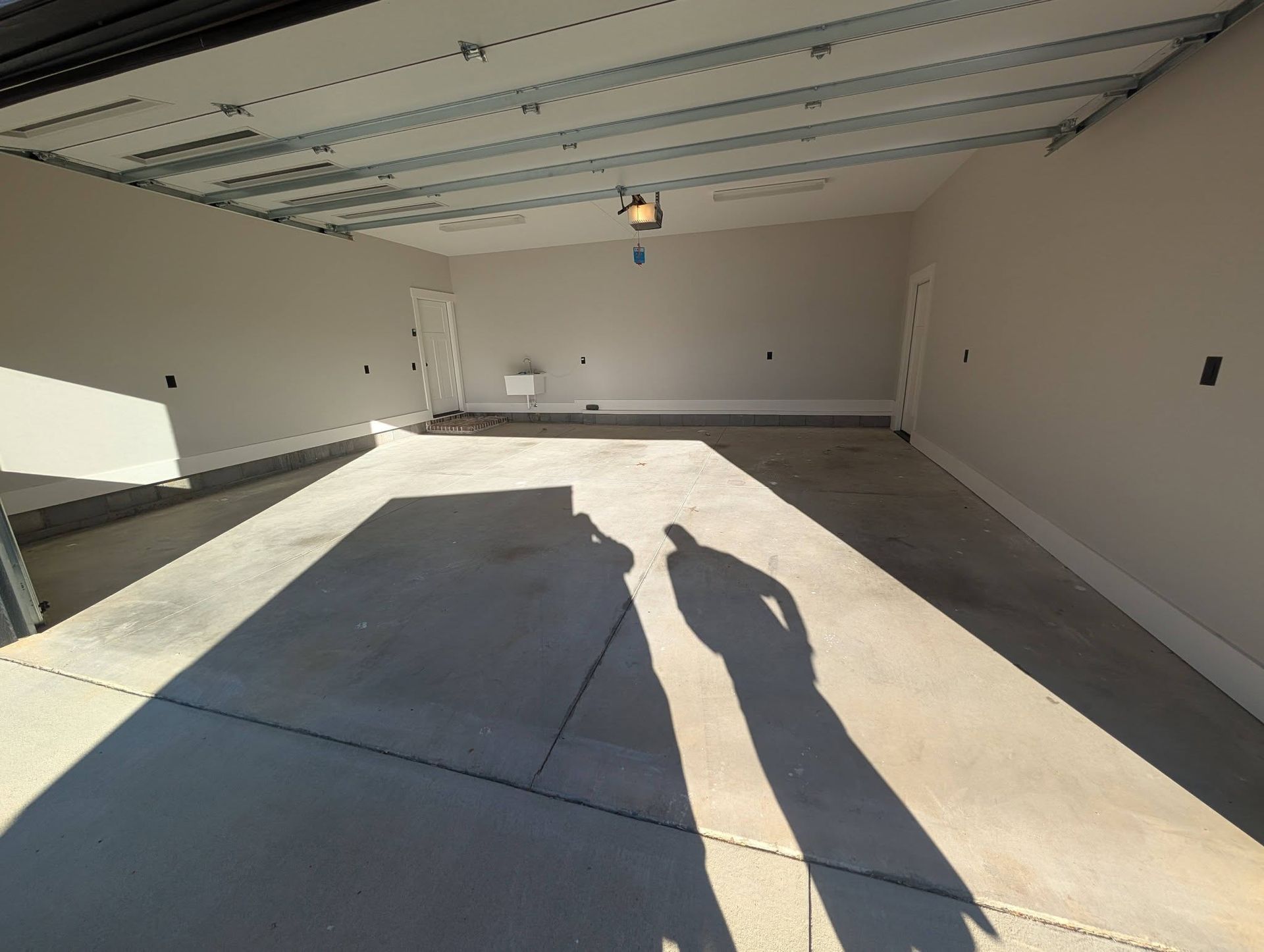 Empty garage with open door, concrete floor, white walls, and a hanging light casting a long shadow.