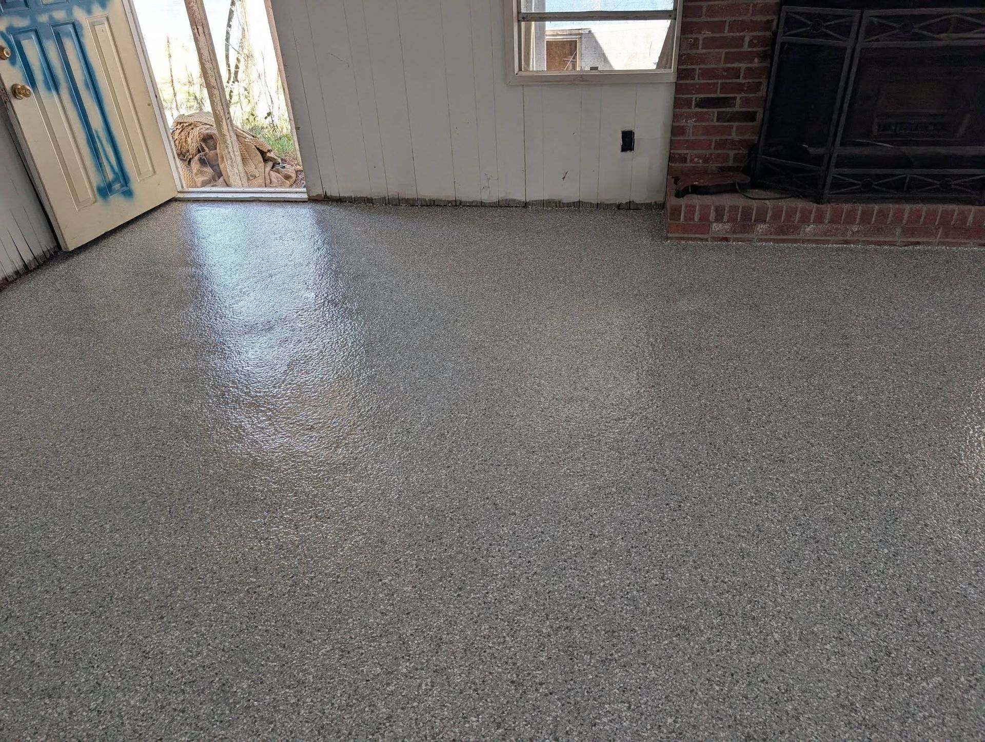 Empty speckled floor in a room with a doorway, window, and fireplace.