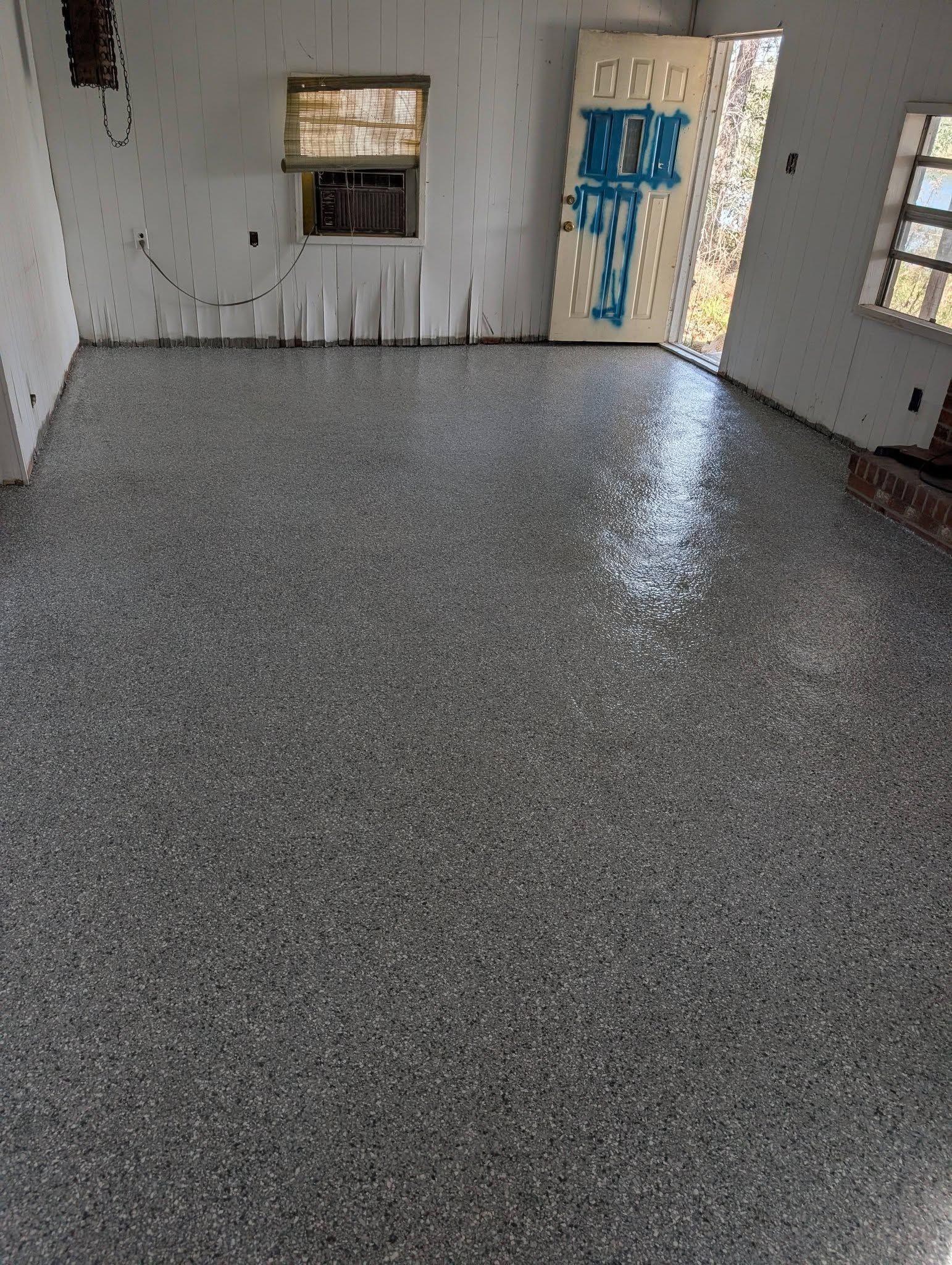 Empty room with speckled gray floor, white walls, and a door marked with blue paint.