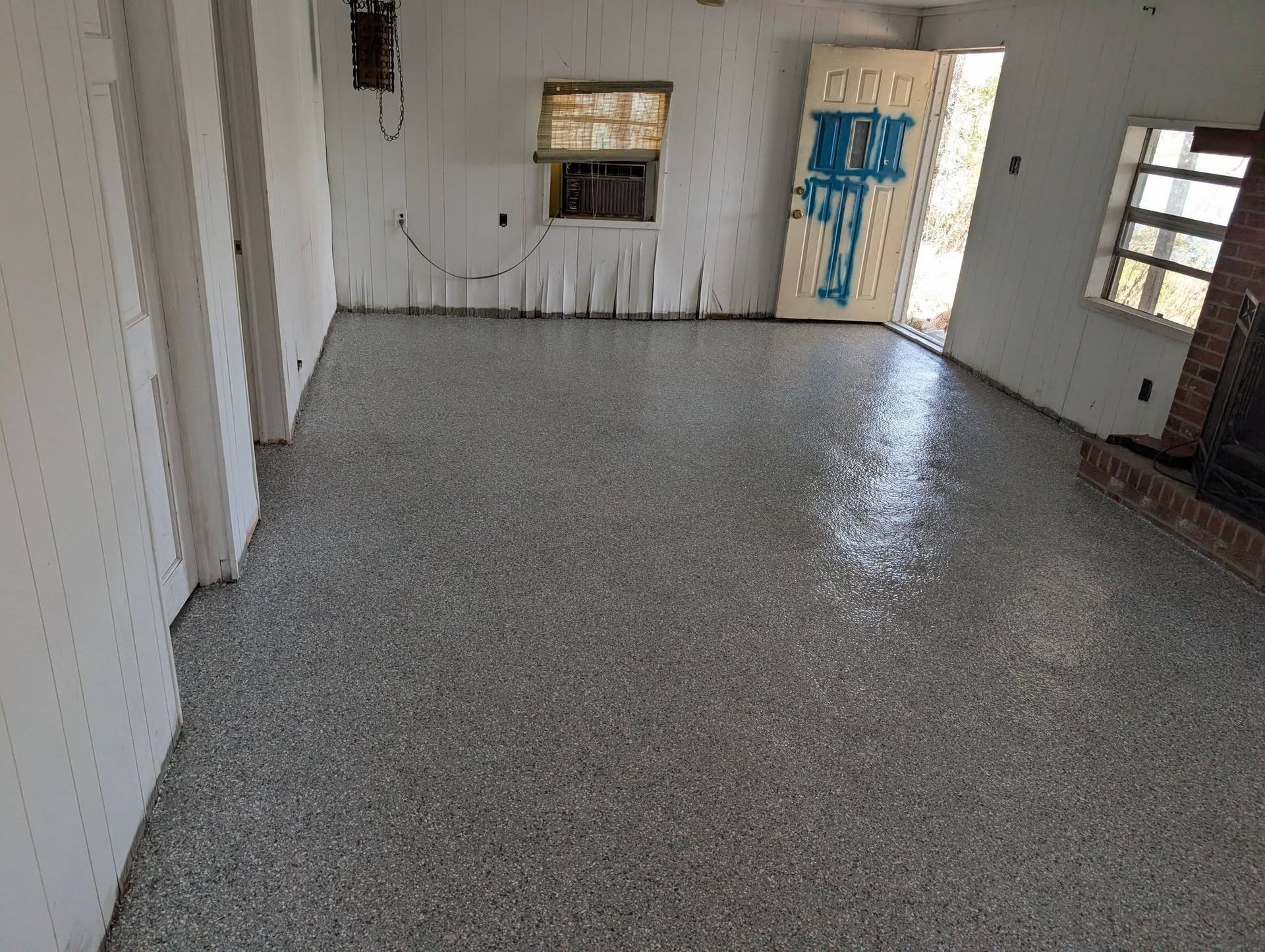 Empty white room with gray speckled floor, two windows, and a door with blue tape on it