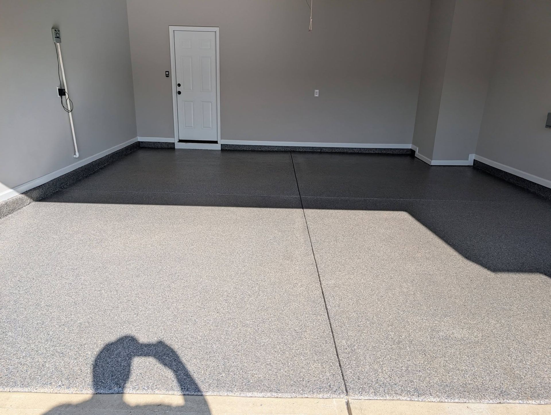 Empty gray room with speckled floor and a white door on the back wall