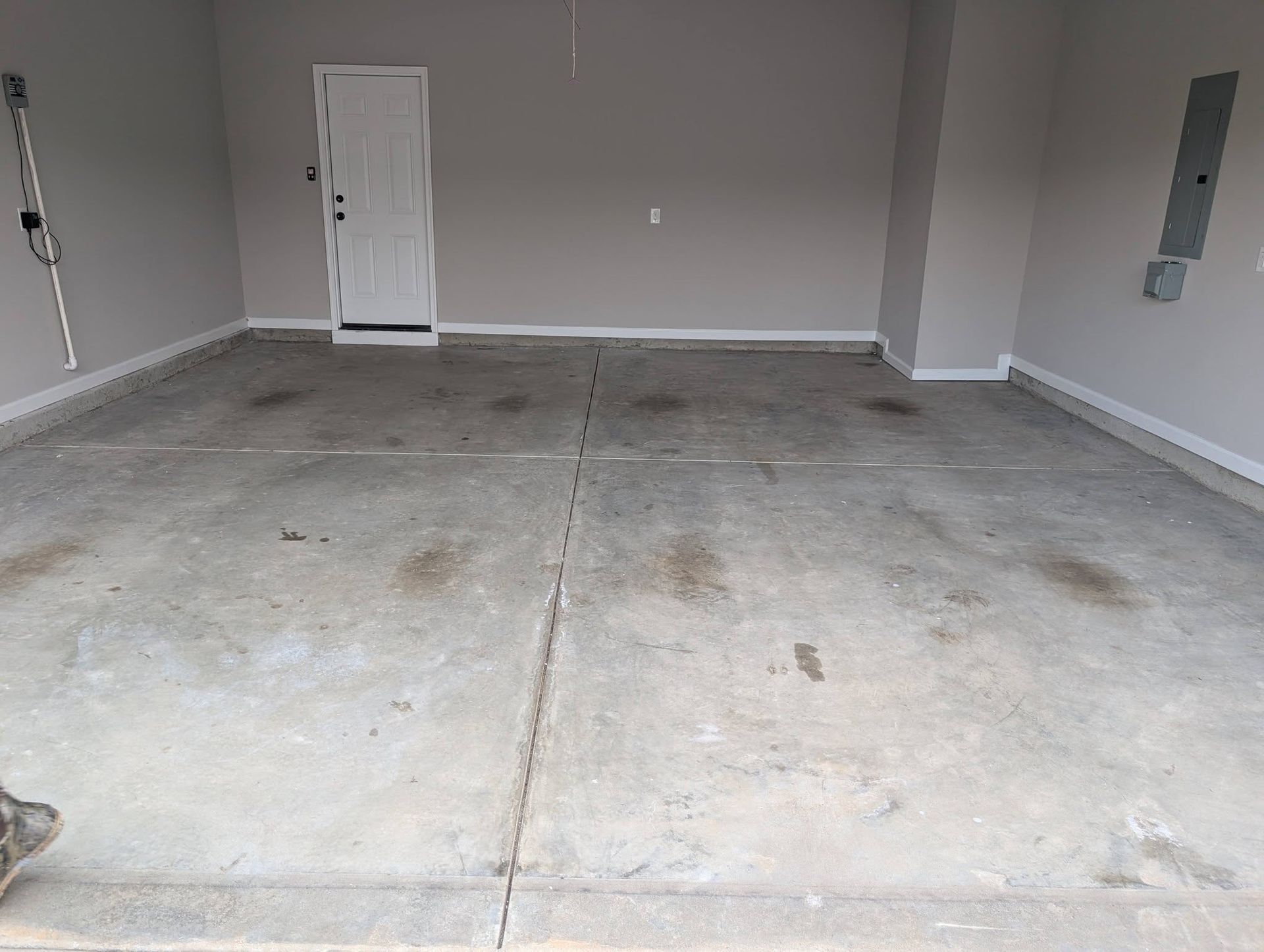 Empty unfinished garage with bare concrete floor and gray walls, viewed from the entrance.