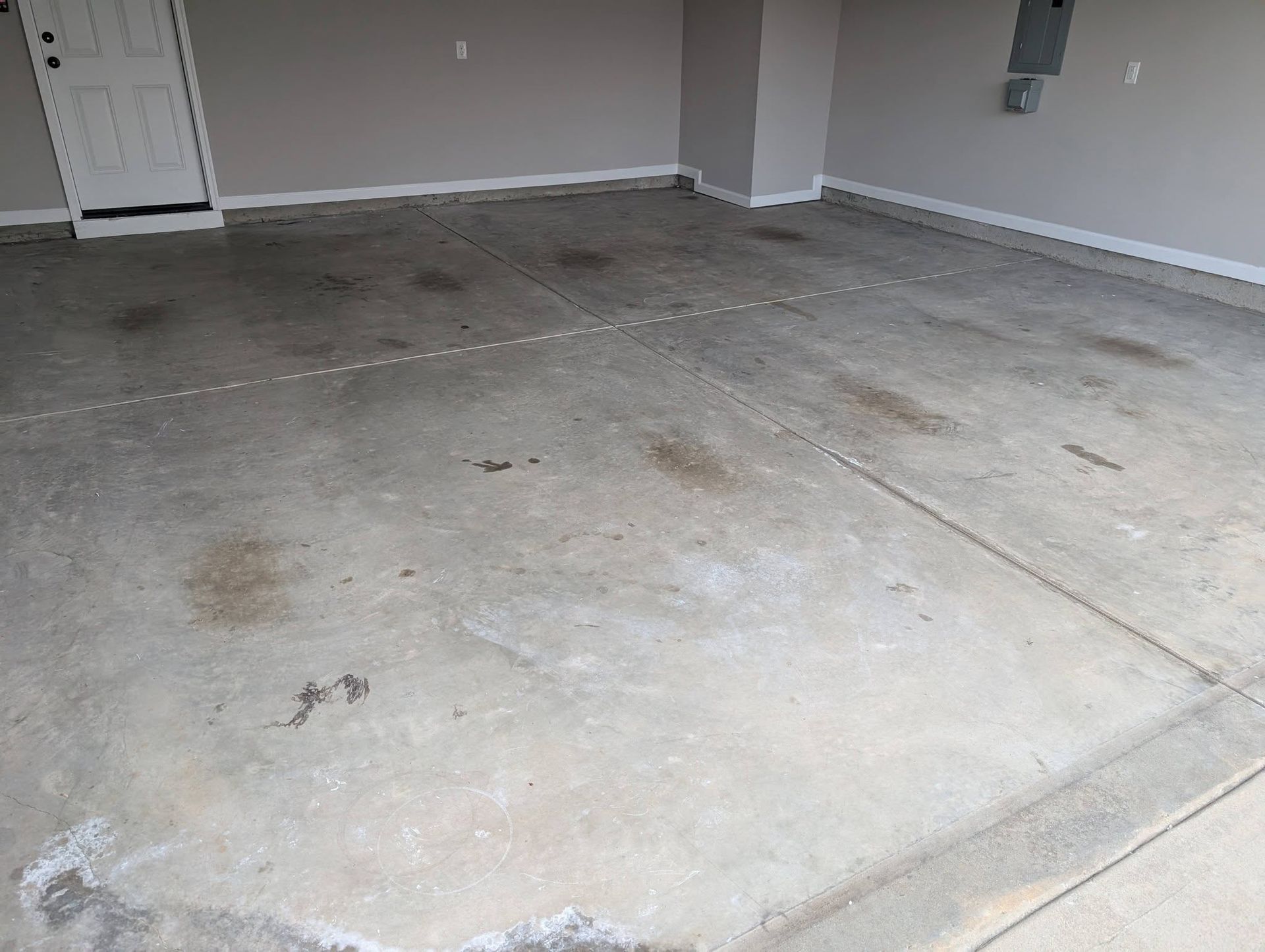 Empty concrete garage floor with stains and a white wall/door in the background