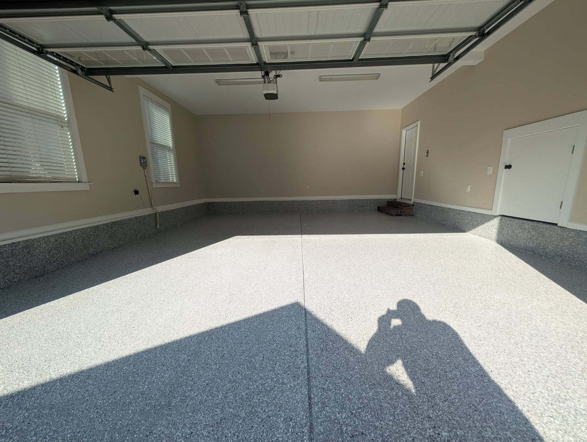 Empty concrete garage with a beige wall, open door, and sunlight casting shadows on the floor.