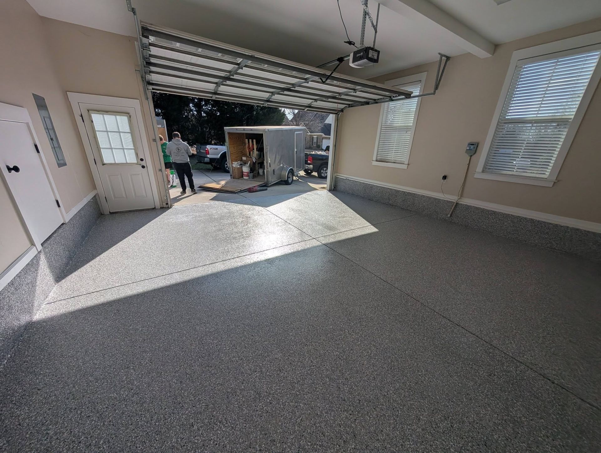 Interior of a garage with open door, gray speckled floor, and two people near the entrance.