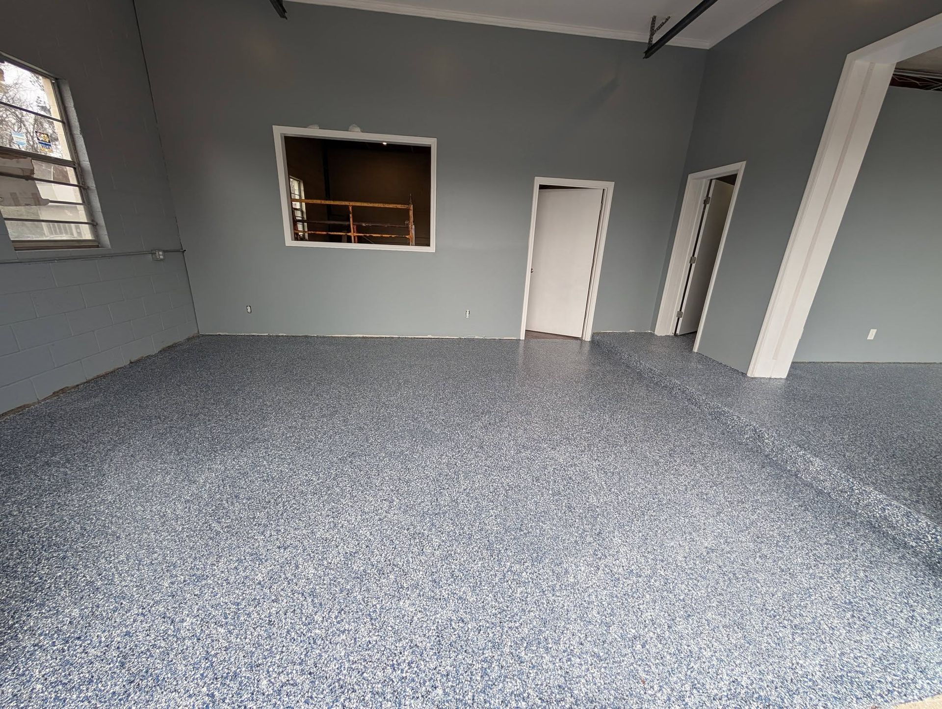 Empty gray carpeted room with gray walls, a window opening, and two white doors