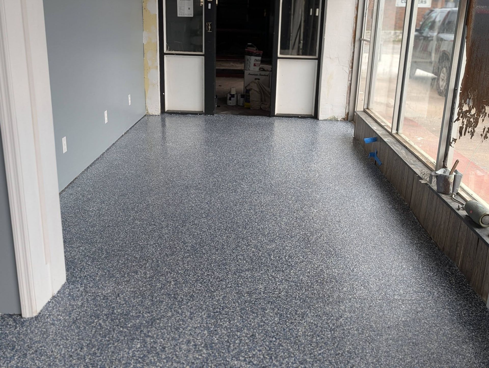 Empty indoor hallway with gray speckled floor and windows along the right wall