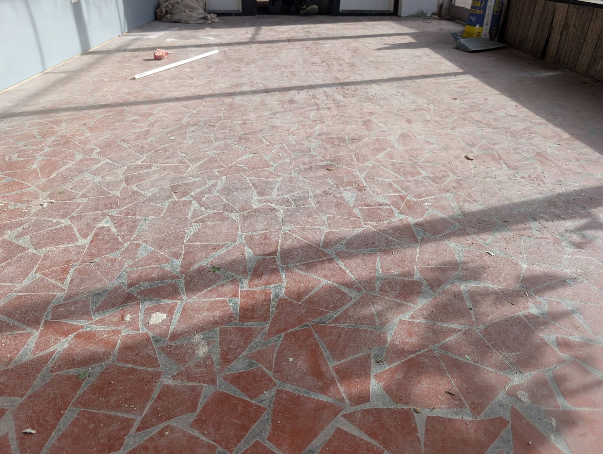 Cracked red-tiled patio in bright sunlight, with long shadows across the ground.